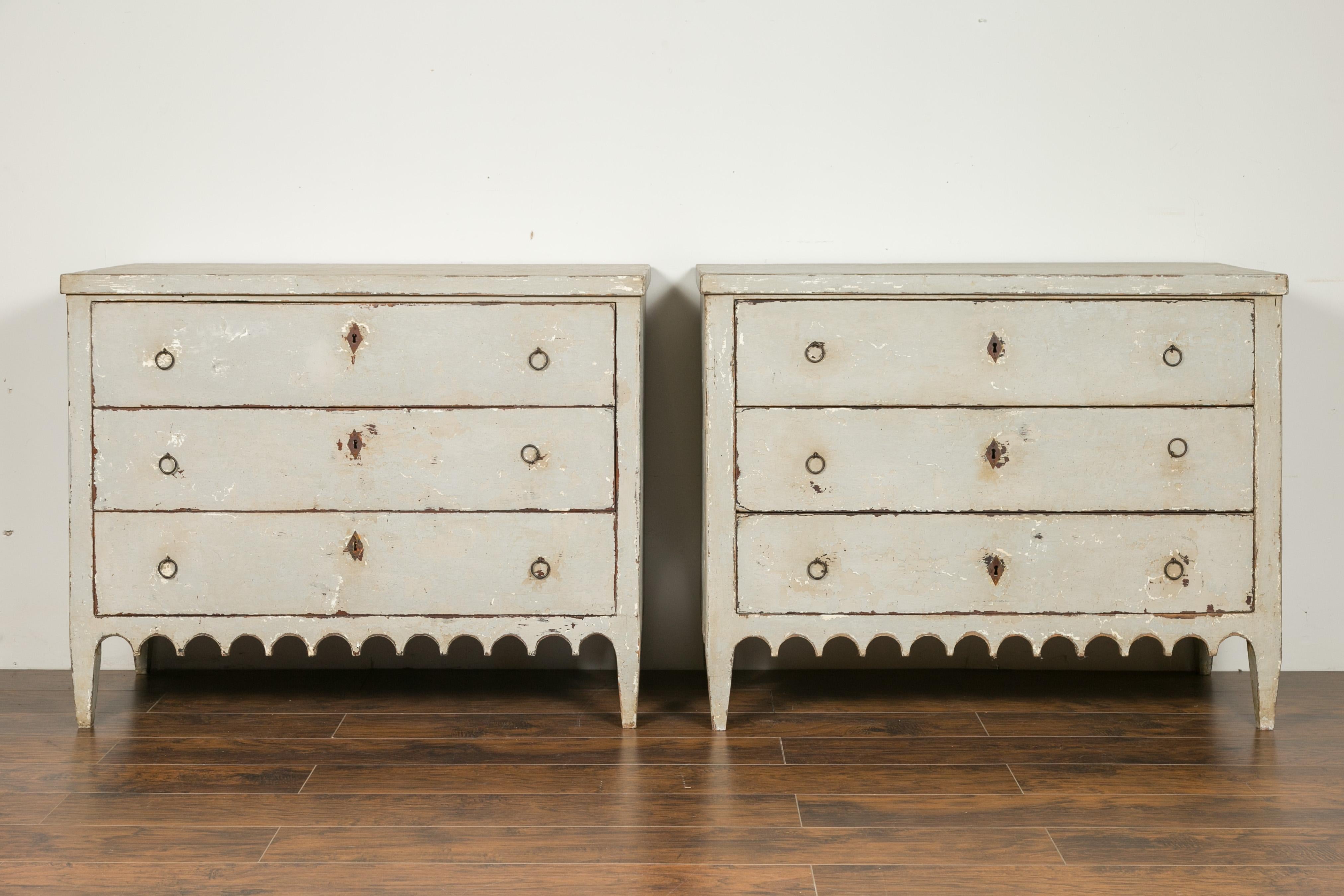 A pair of Portuguese distressed grey painted wooden three-drawer commodes from the late 19th century with scalloped aprons. Created in Portugal during the third quarter of the 19th century, each of this pair of chest-of-drawers features a