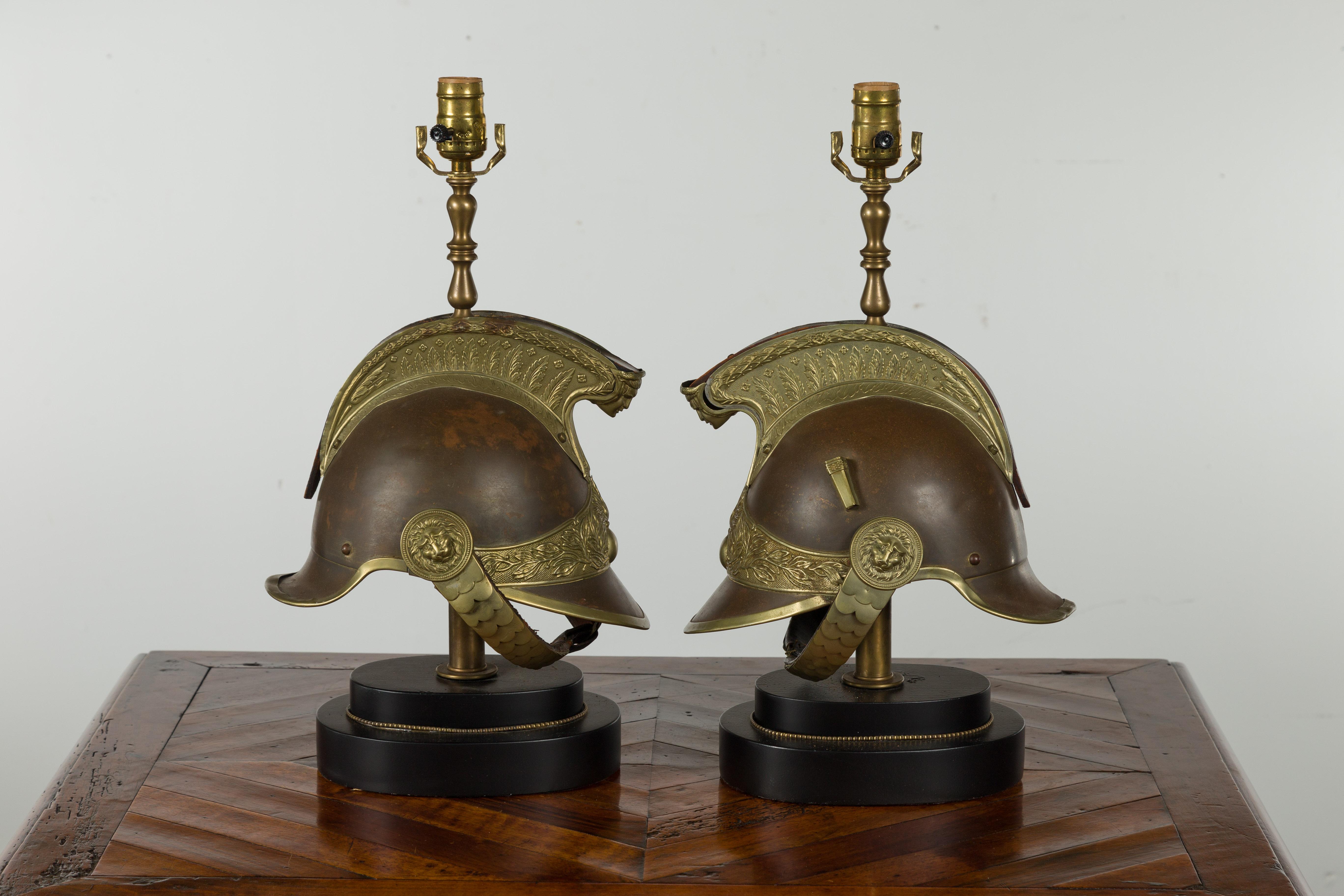 A pair of brass helmet table lamps from the late 19th century, mounted on black oval bases. Created during the last quarter of the 19th century, each of this pair of table lamps captures our attention with its legionary helmet mounted on a black