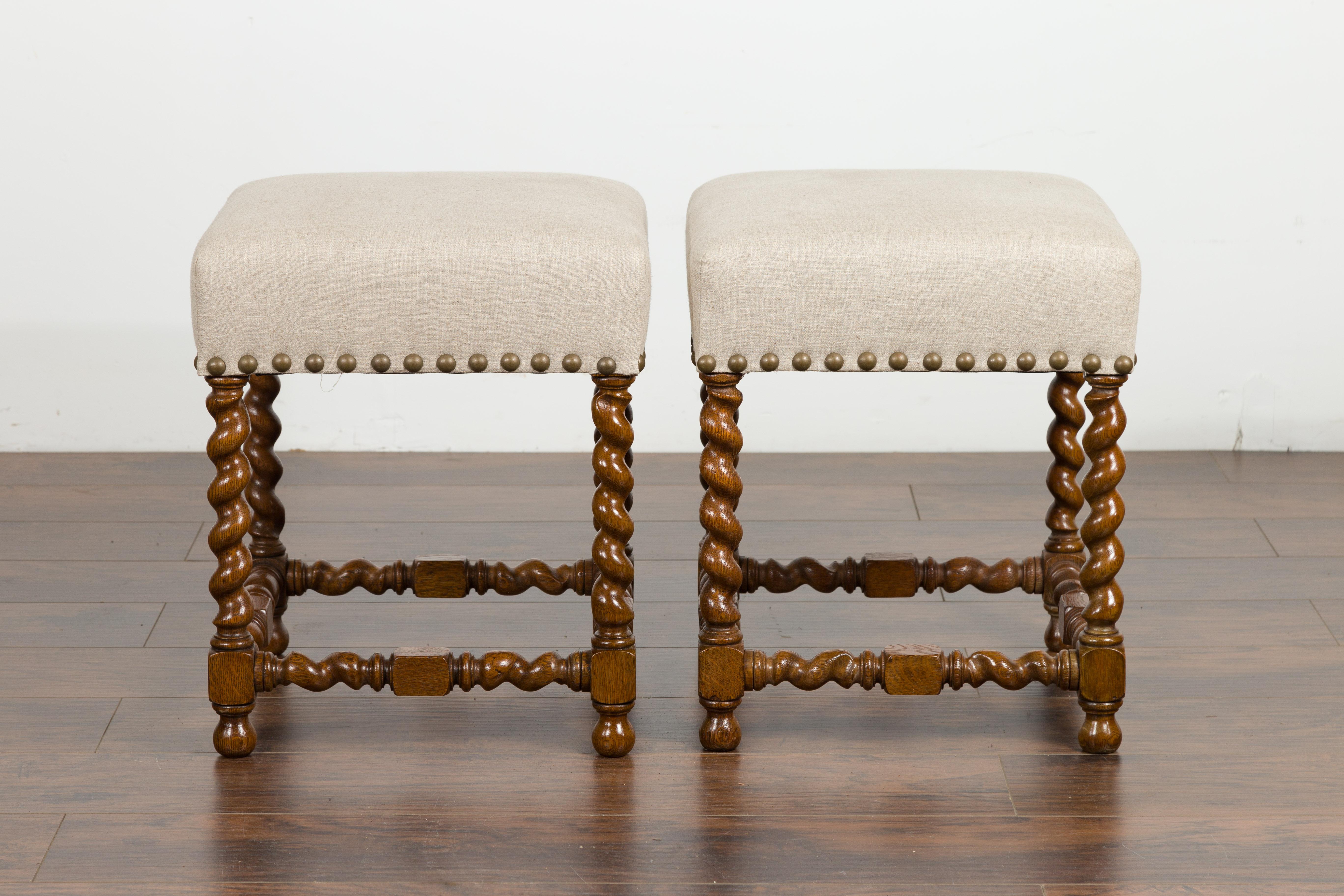 A pair of English oak barley twist stools from the late 19th century, with new upholstery. Created in England during the last quarter of the 19th century, each of this pair of stools features a square top newly recovered with a neutral-toned linen