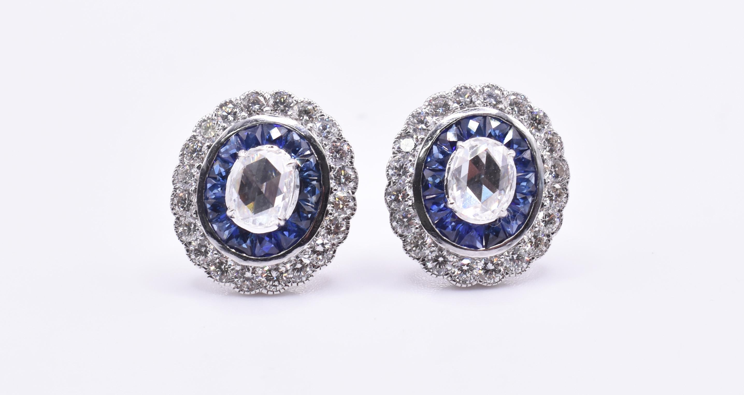 For sale is a good quality pair of 18k Art Deco style white gold diamond and sapphire stud earrings, featuring a stunning rose cut diamond to the centre of each earring, surrounded by a halo of 14 blue sapphires, with a further 20 round cut diamonds