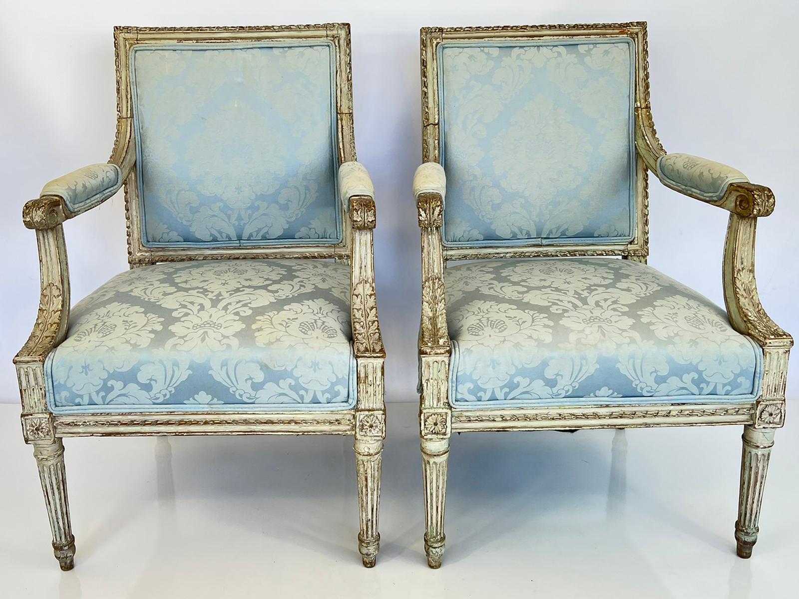 Pair of Louis XVI fauteuils, having their original putty-gray painted finish. Each armchair has a squared, padded backrest, in a channeled frame with a gadrooned border. The downswept armrests with padded elbow cushions, ending in scrolls, and