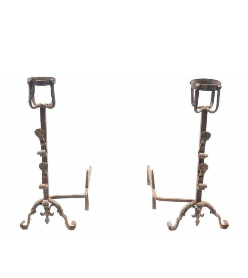 Antique French hand forged wrought iron andiron pair, basket style tops, fleur-de-lis lower finial, split from the solid tapering iron columns, which have brackets attached to front with heavy iron rivets for holding tools, mounted on an arched iron