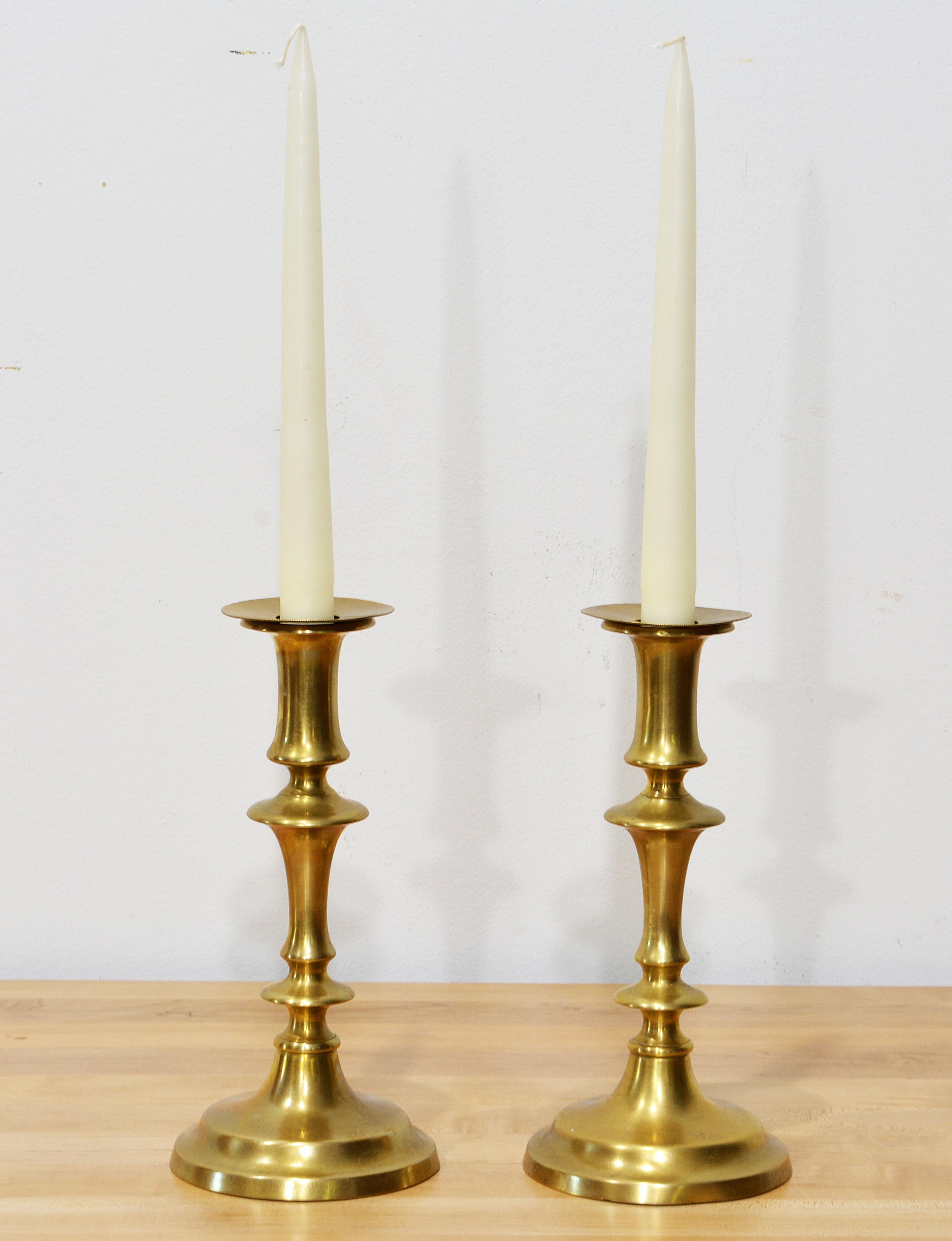 This pair of English 18th century Queen Anne brass candle sticks feature beautifully shaped stems on round softly stepped bases. The brass wheb polished shows an attractive mellow shine reflecting years of use and maintenance. They come with drip