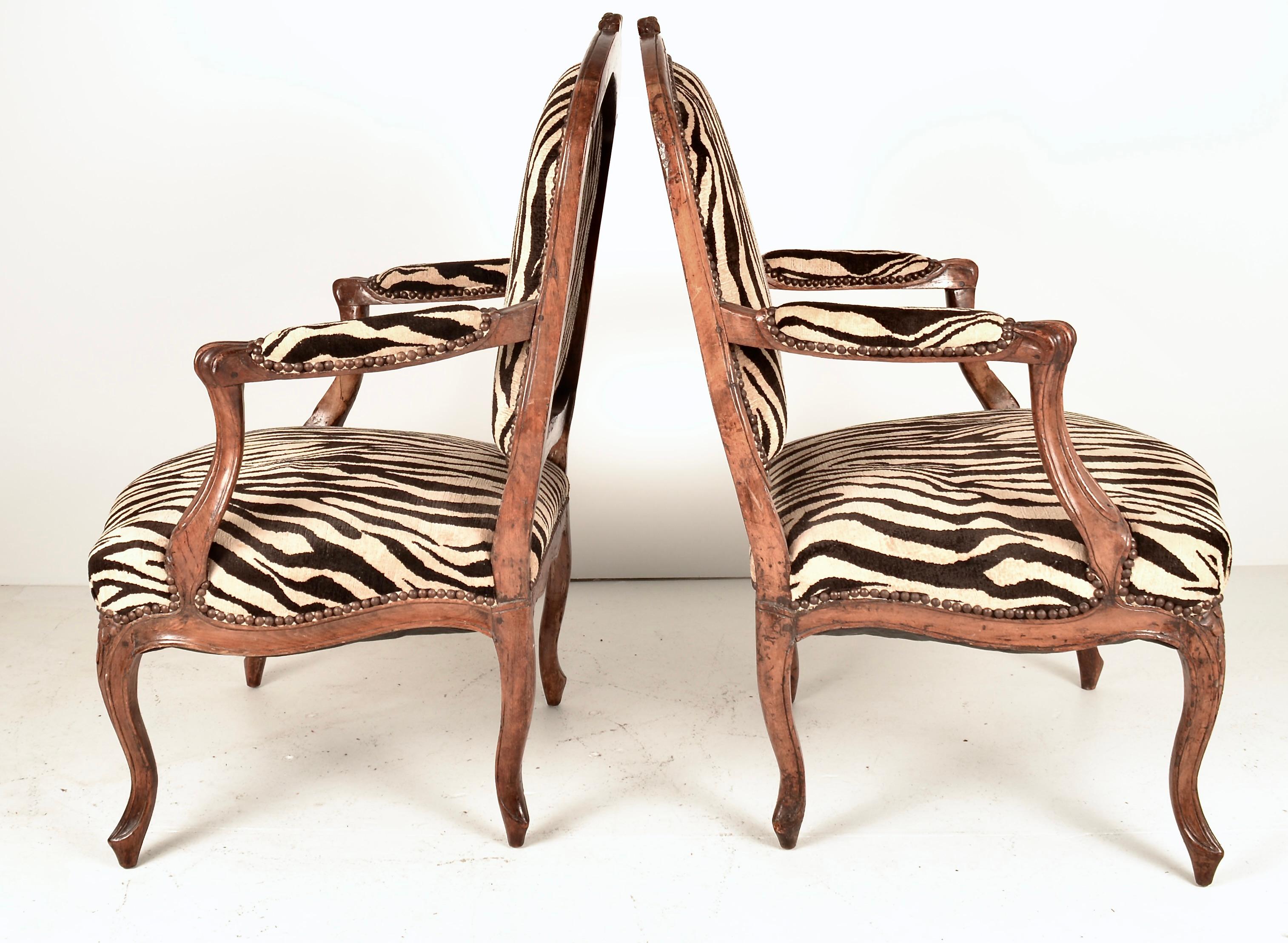 A handsome pair of French open arm chairs. Lovely patina on hand-carved fruitwood frames. Newly upholstered in a quality jacquard velvet in a zebra pattern. Quality, sturdy chairs in very fine condition. 
