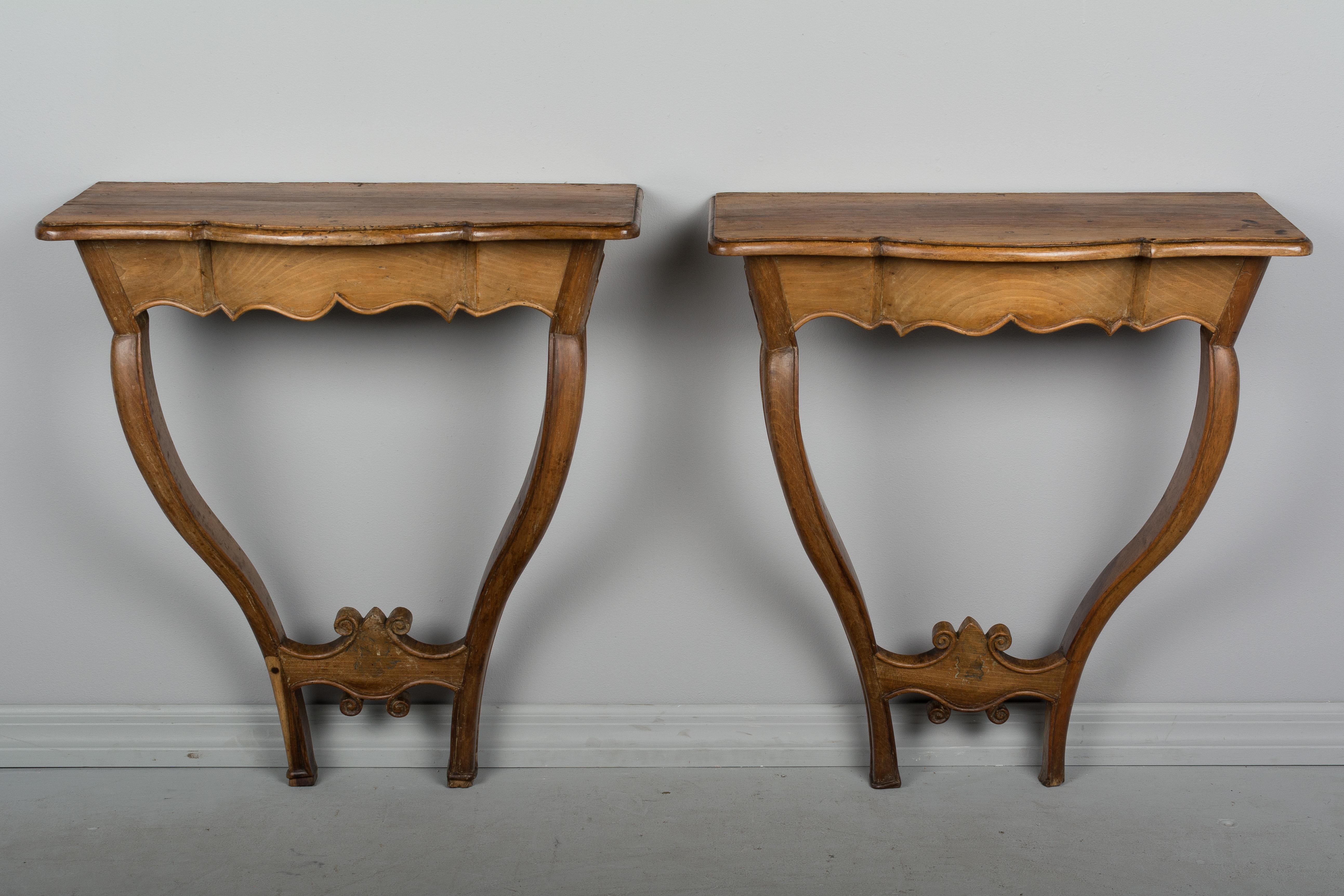 A pair of 18th century French Louis XV style console tables made of solid walnut with nice patina and waxed finish. Simple in design, with elegant curved legs and scalloped apron. These consoles once had a painted finish and have signs of a missing