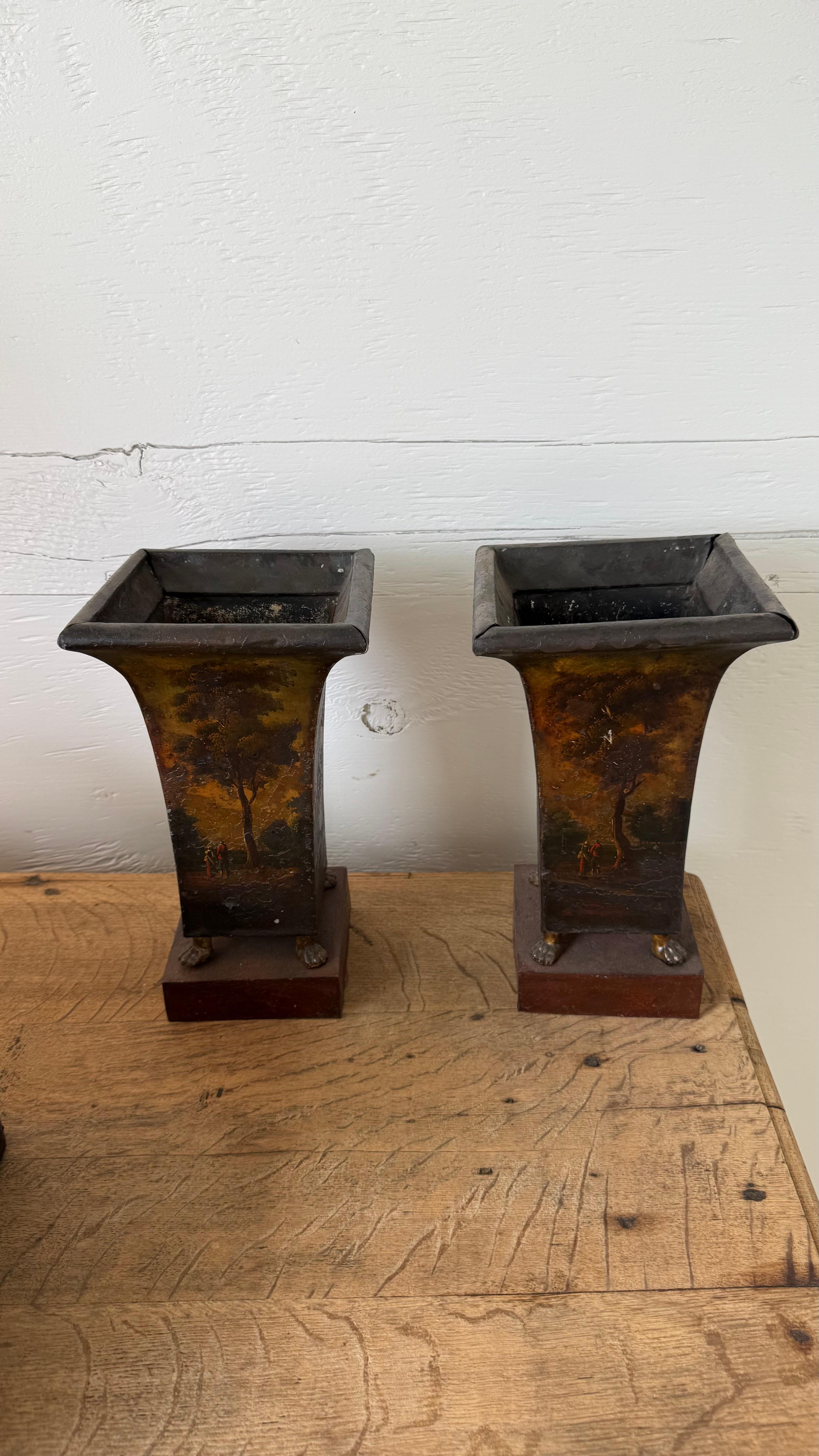 Elegantly aged and rich with historical charm, this pair of 18th century painted tole urns brings a refined touch of antique European decor to any interior. Handcrafted from tole (tinned metal) and adorned with remnants of their original painted