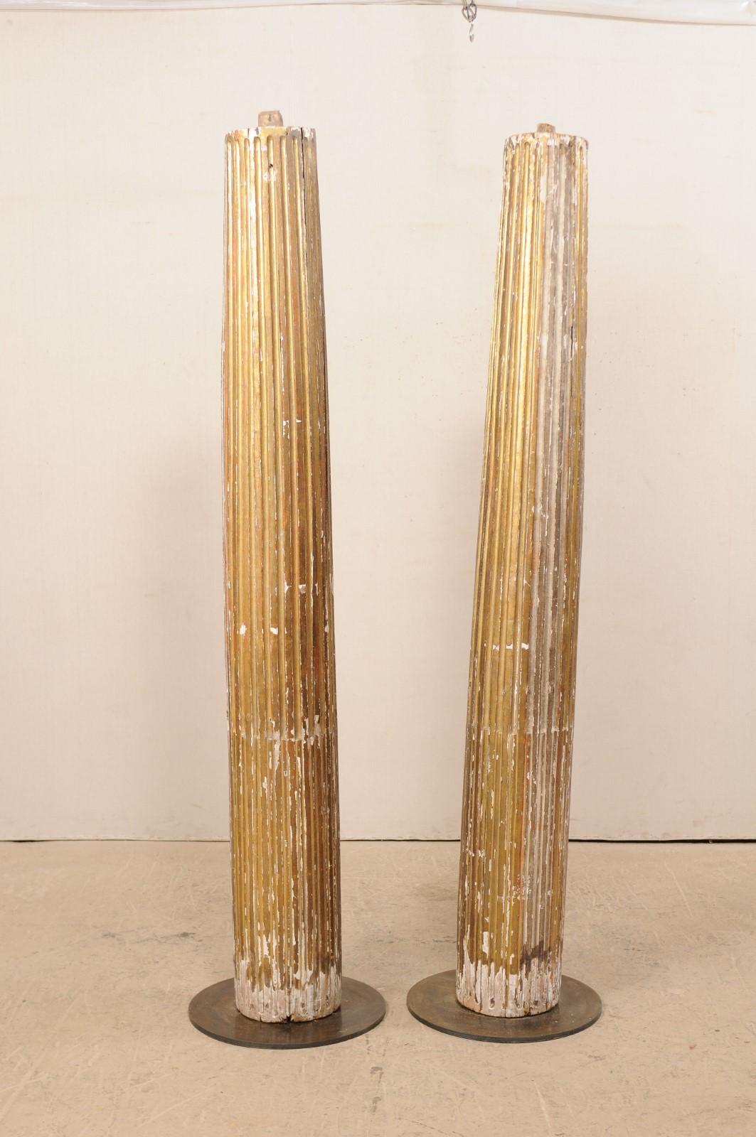 A pair of Italian fluted and giltwood columns from the 18th century. This antique pair of tall architectural columns from Italy feature fluted, and rounded bodies, tapering slightly towards their top, with a fabulous old chippy patina and gilt. Each