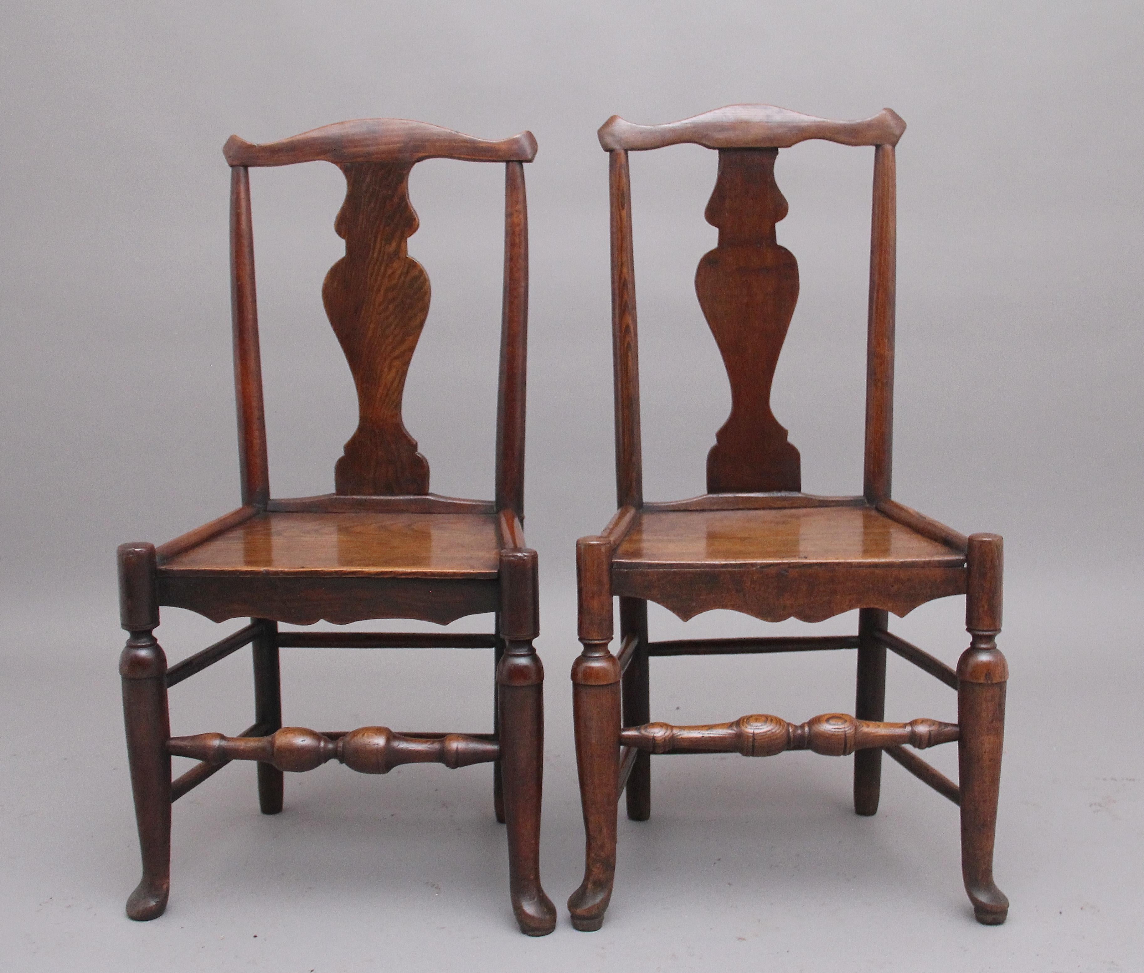 A pair of mid 18th Century elm side chairs from the Georgian period, having a shaped rail above a decorative shaped splat with turned side supports, wonderfully figured plank seat with a shaped apron, raised on turned legs united with side, back and