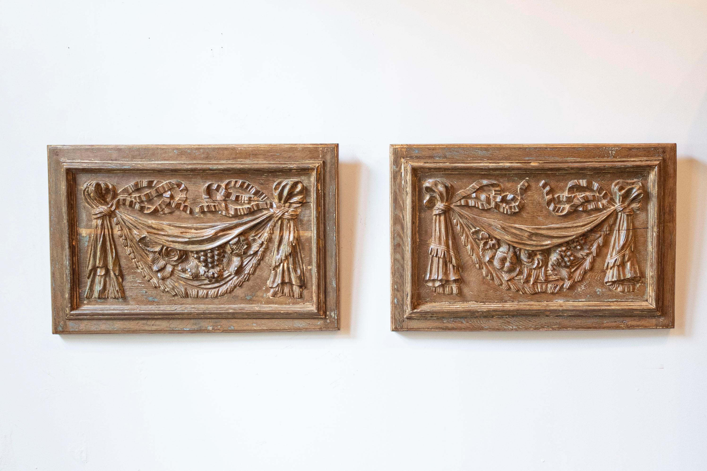 Pareja de paneles decorativos franceses de madera tallada a mano del siglo XVIII, con guirnaldas de cintas, flores y frutas. Nacidos en Francia durante el Siglo de las Luces, cada uno de este par de paneles arquitectónicos de madera presenta un