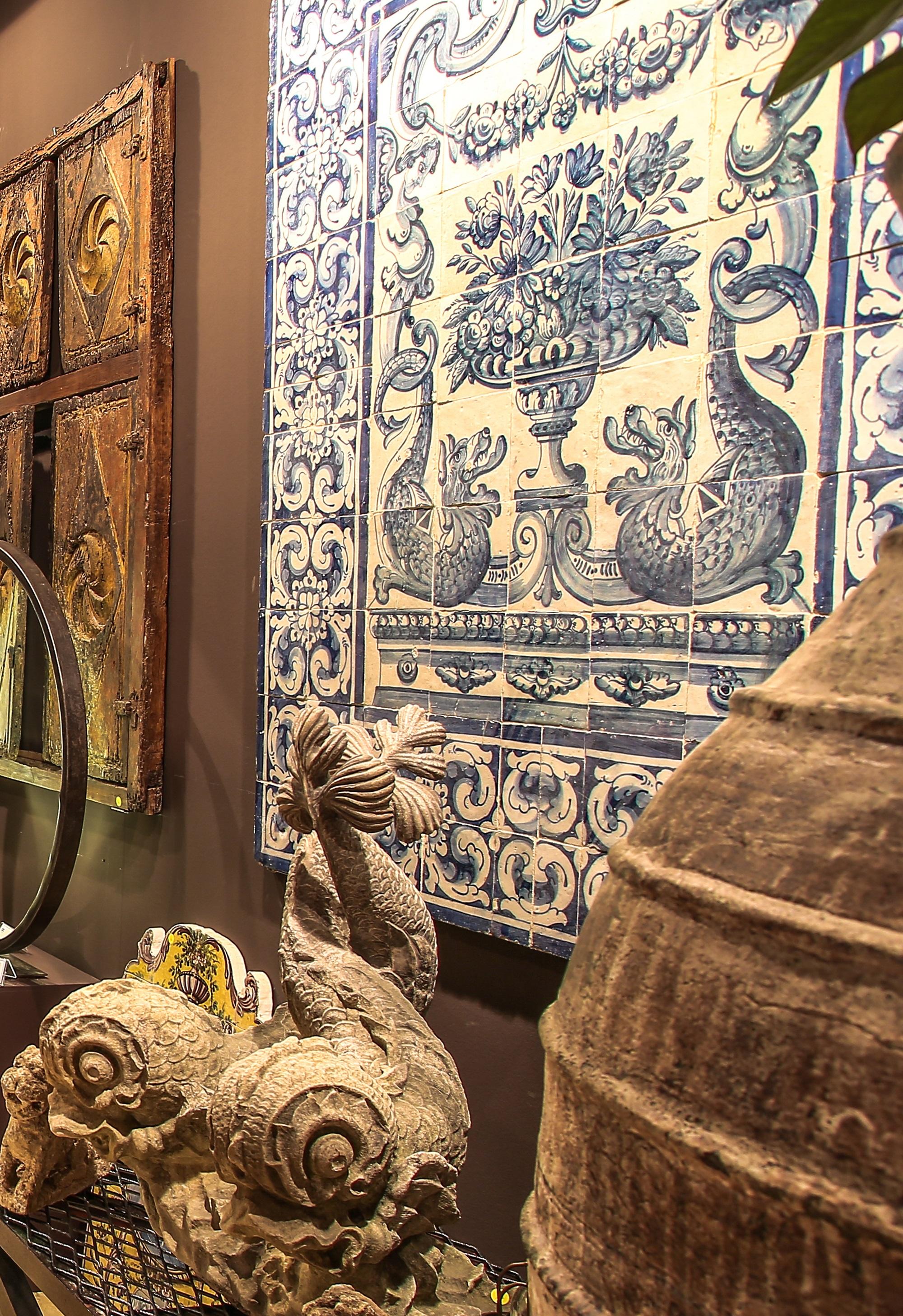 1st half of the 18th century produced in Lisbon.
Painting in cobalt blue over white glaze, mimicking Chinese porcelain and following Delft fashion of the time. 
Two flower baskets surrounded renaissance dolphins and caryatids are framed by a two