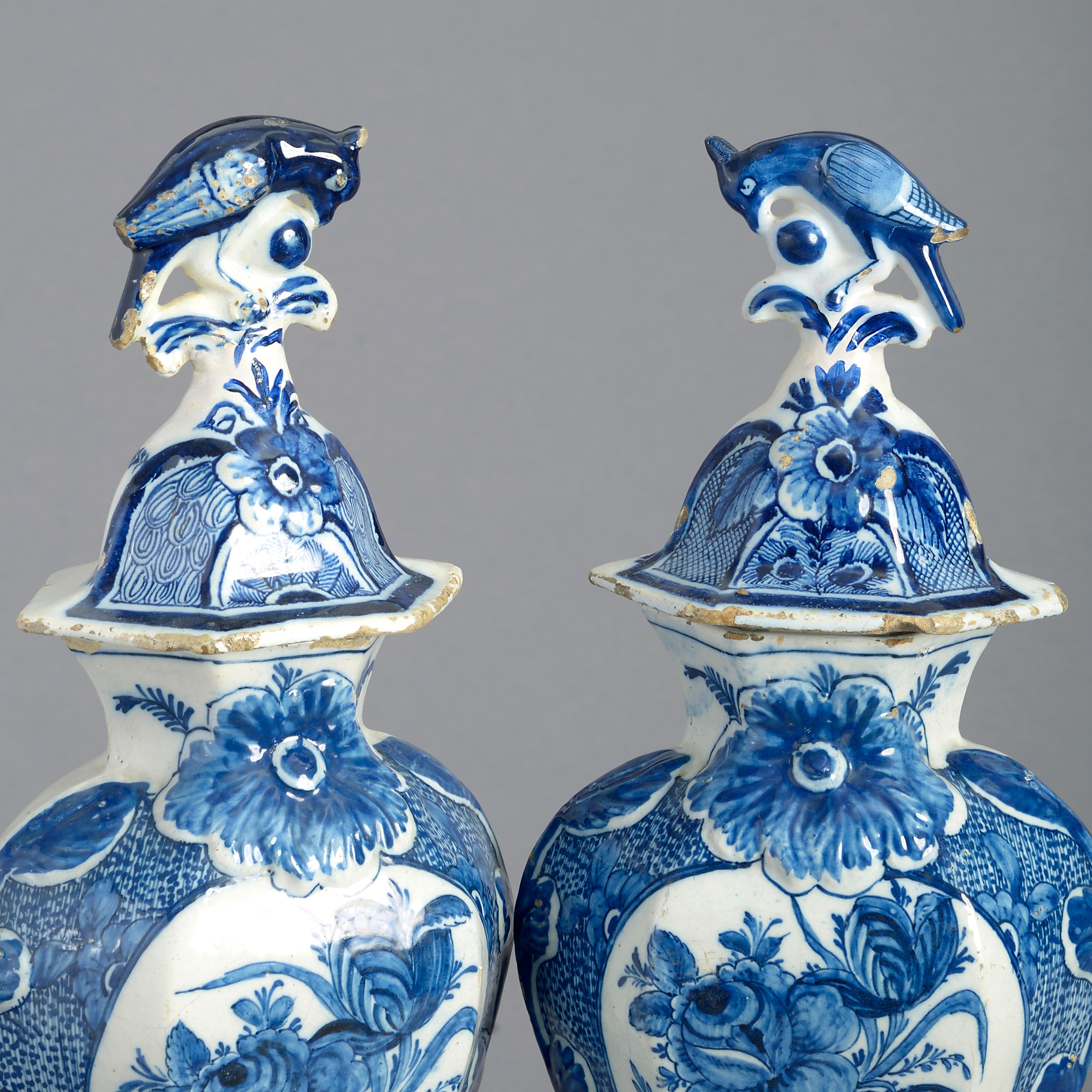 A good pair of late 18th century blue and white glazed delft pottery vases and covers, the lids with parrot finials, the shaped bodies having floral cartouches.