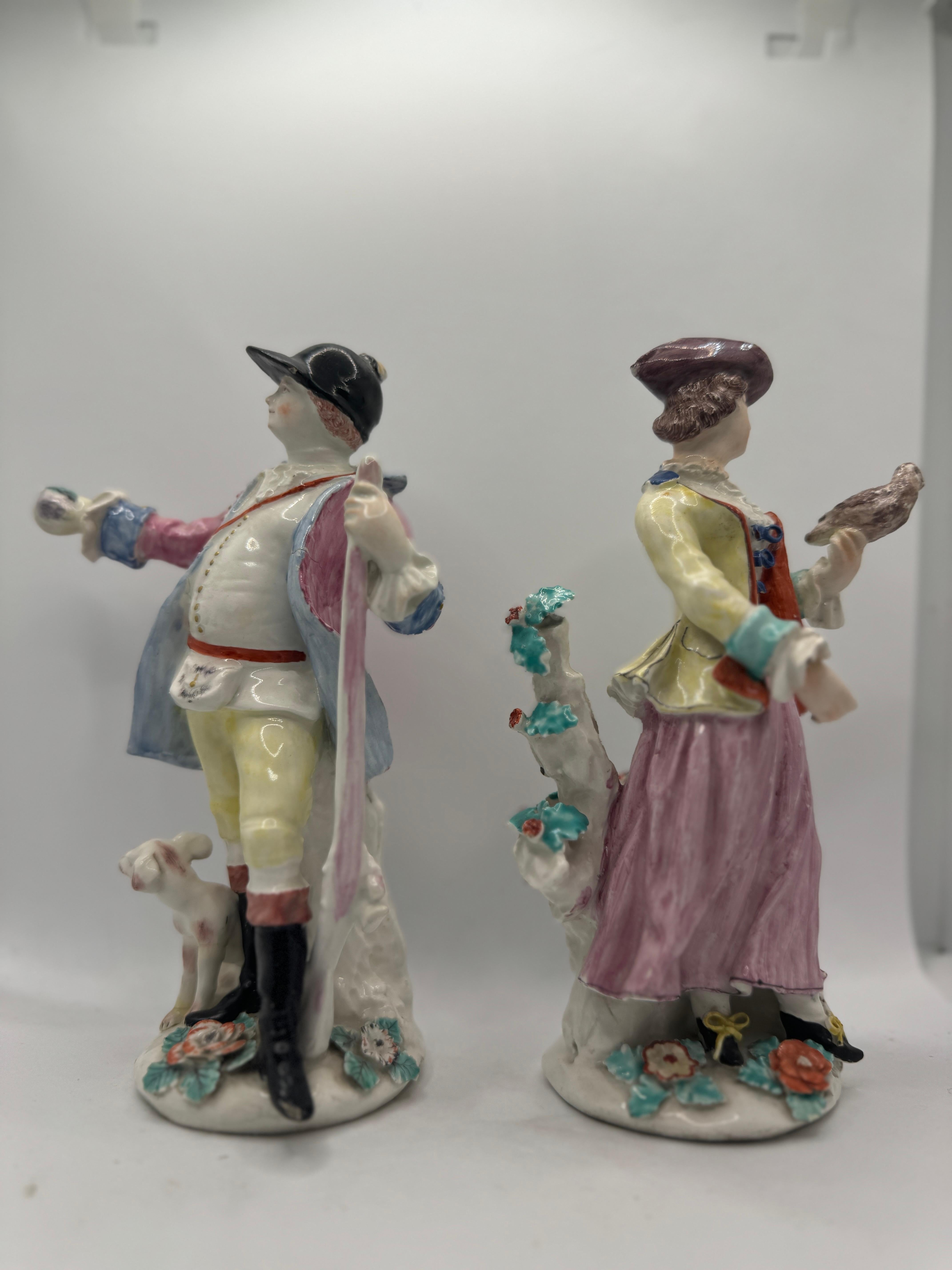 Pair of 18th Century English Bow Figures of Hunter and Companion (a Lady Falconer) , circa 1755, he modelled to the left with a gun leaning against his left arm, seated on a rock with a dog at his feet, she modelled to the right with a gun in her