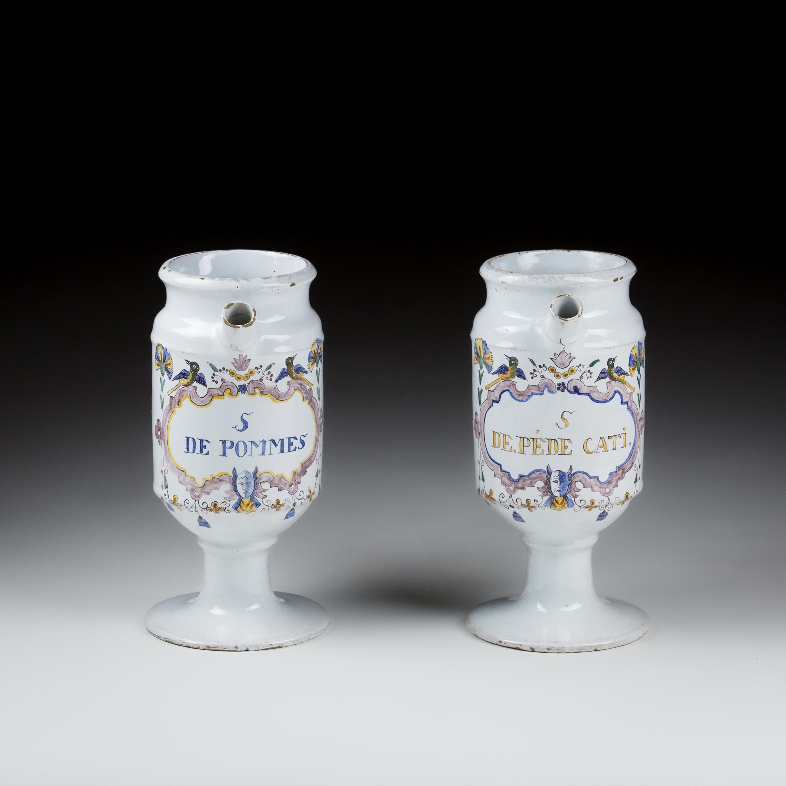 Paire de jarres à sirop en faïence de Bruxelles polychrome à bec verseur. Peint en bleu, jaune et manganèse, avec un cartouche exubérant composé de masques et d'oiseaux. L'une porte l'inscription S de Pommes, l'autre S DE.Pede Cati. Paire similaire