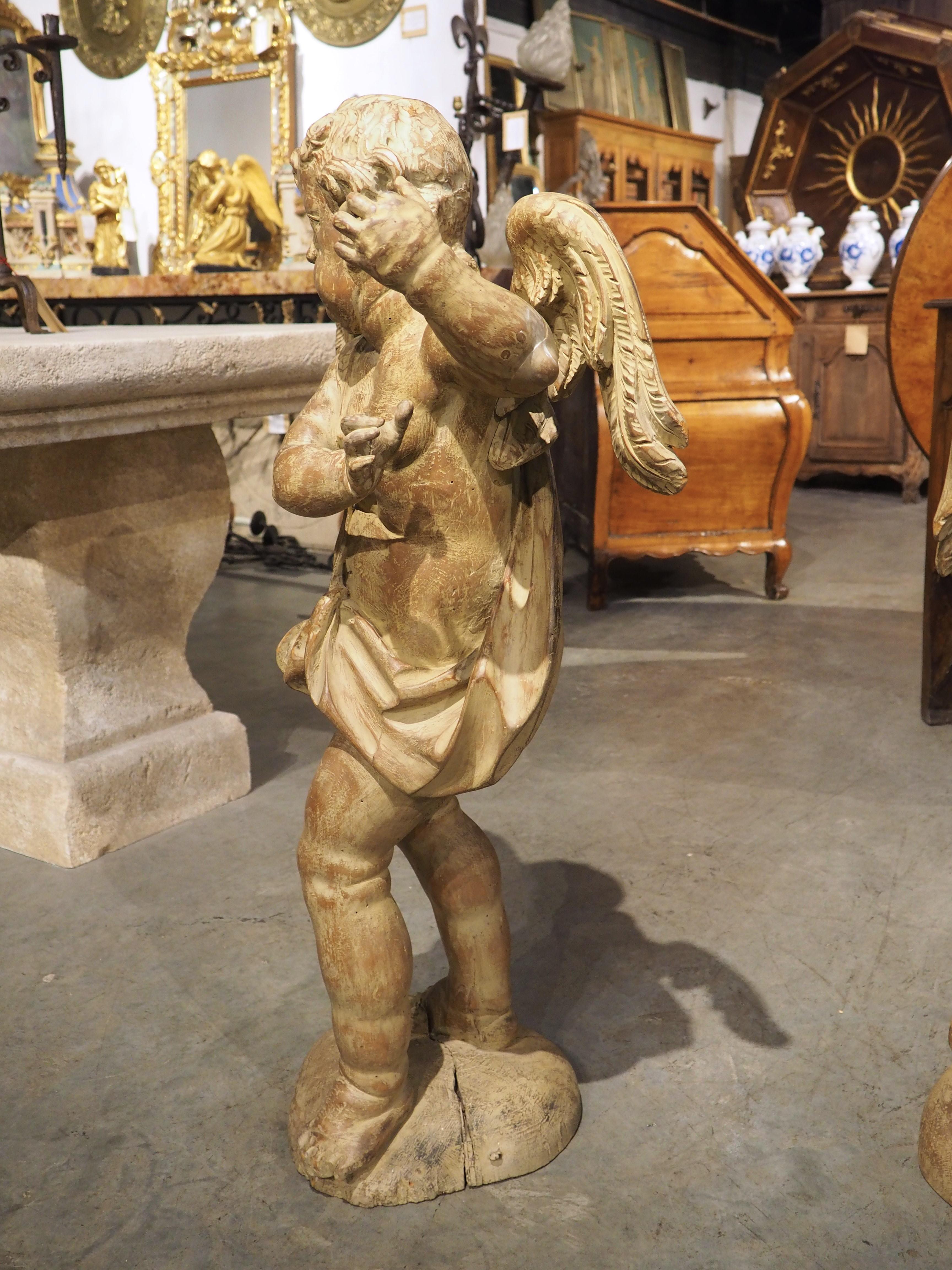 Originally from 18th-century Italy, this pair of winged cherubs were hand-carved from wood as reflections of each other, meaning that their bodies are orientated as mirror images. Both figures have been shown with their arms held high, positioned as