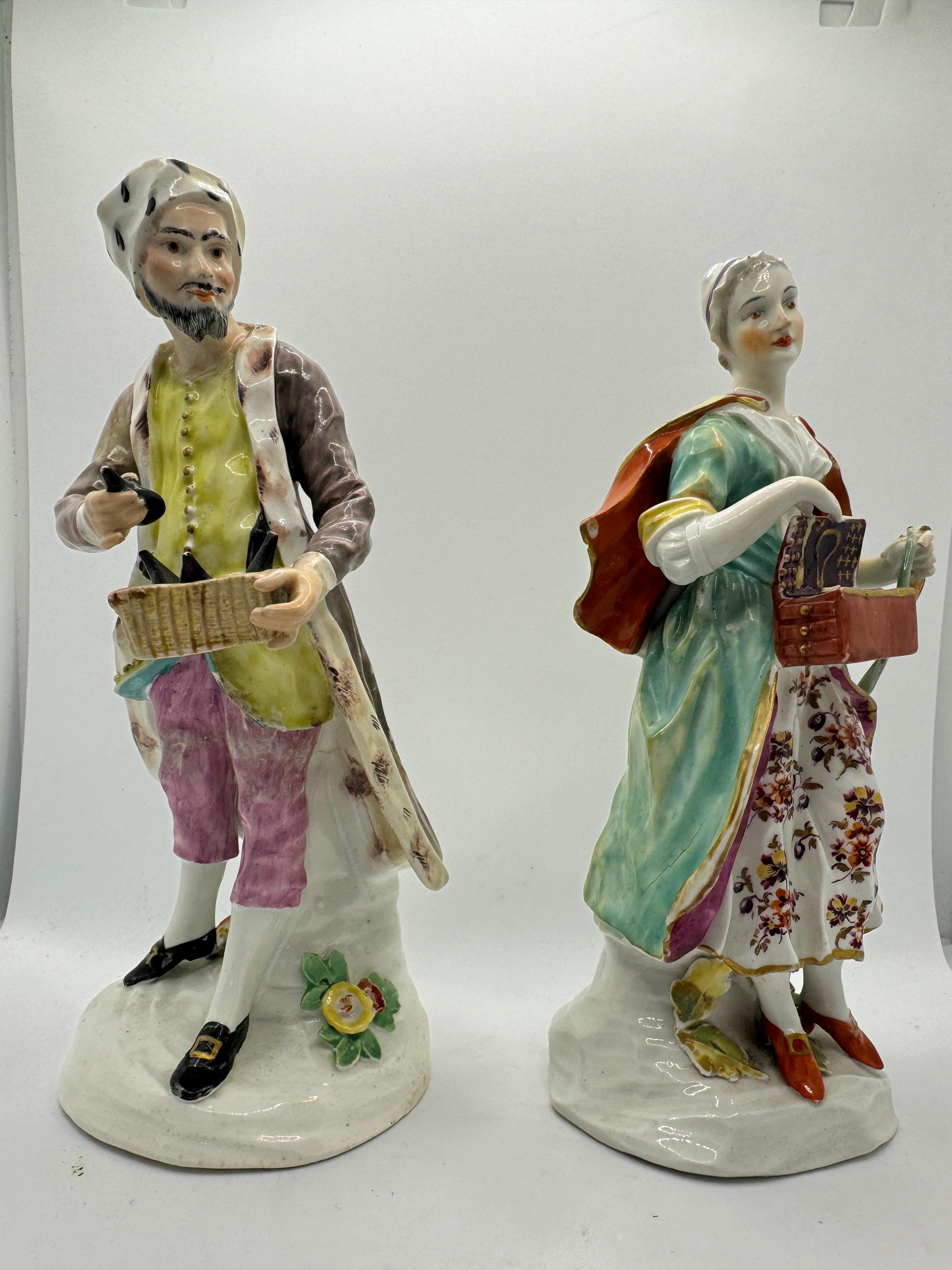 Pair of 18th Century Derby Figures of 'Jewish Pedlar and Companion' , circa 1760 , made from polychrome enamelled porcelain, both depicted in colourful pink and yellow outfits decorated with flowers, he wearing a fur-trimmed hat and carrying a