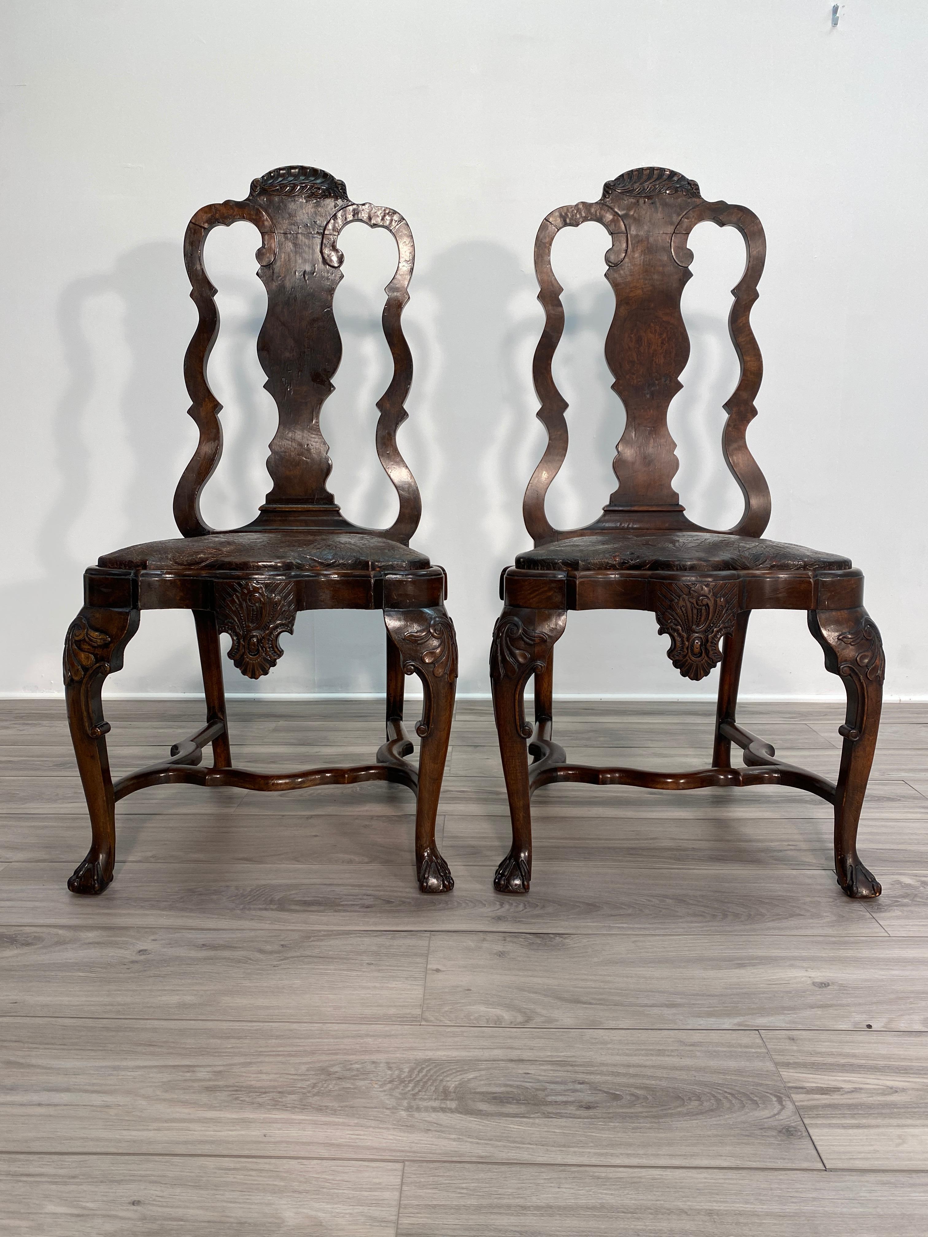 Wonderful pair of heavily carved 18th century Dutch side chairs. Both chairs have shell carvings in the crest rails. The knees are carved with Rococo themed acanthus patterns, rounding into cabriolet legs terminating in carved claw feet. The legs