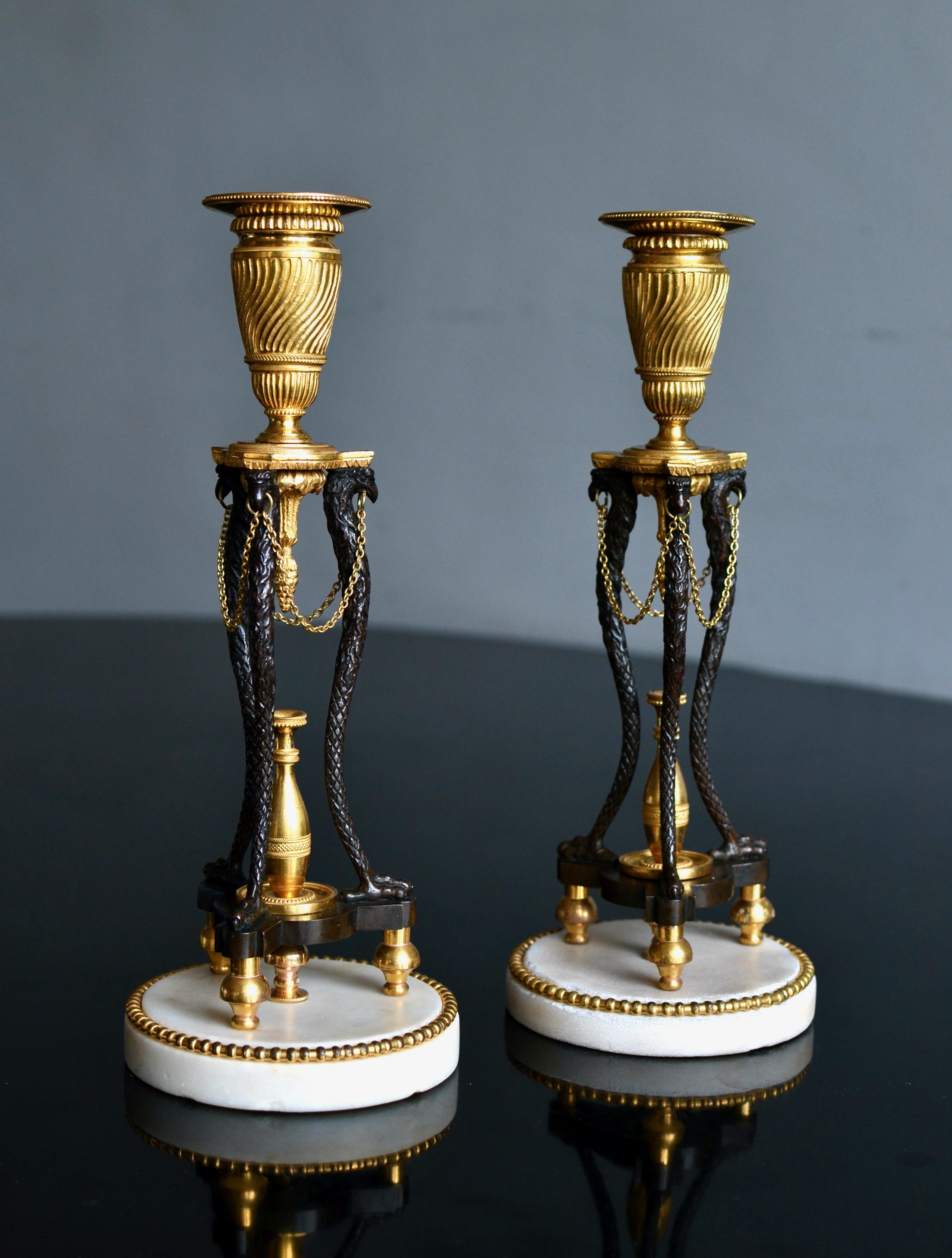 A rare and elegant pair of English candlesticks, probably made circa 1799 by the workshop of Matthew Boulton (1728-1809) after a design by William Chambers (1723-1796). Gilt and patinated bronze, the base of Carrara marble. Candle holders are