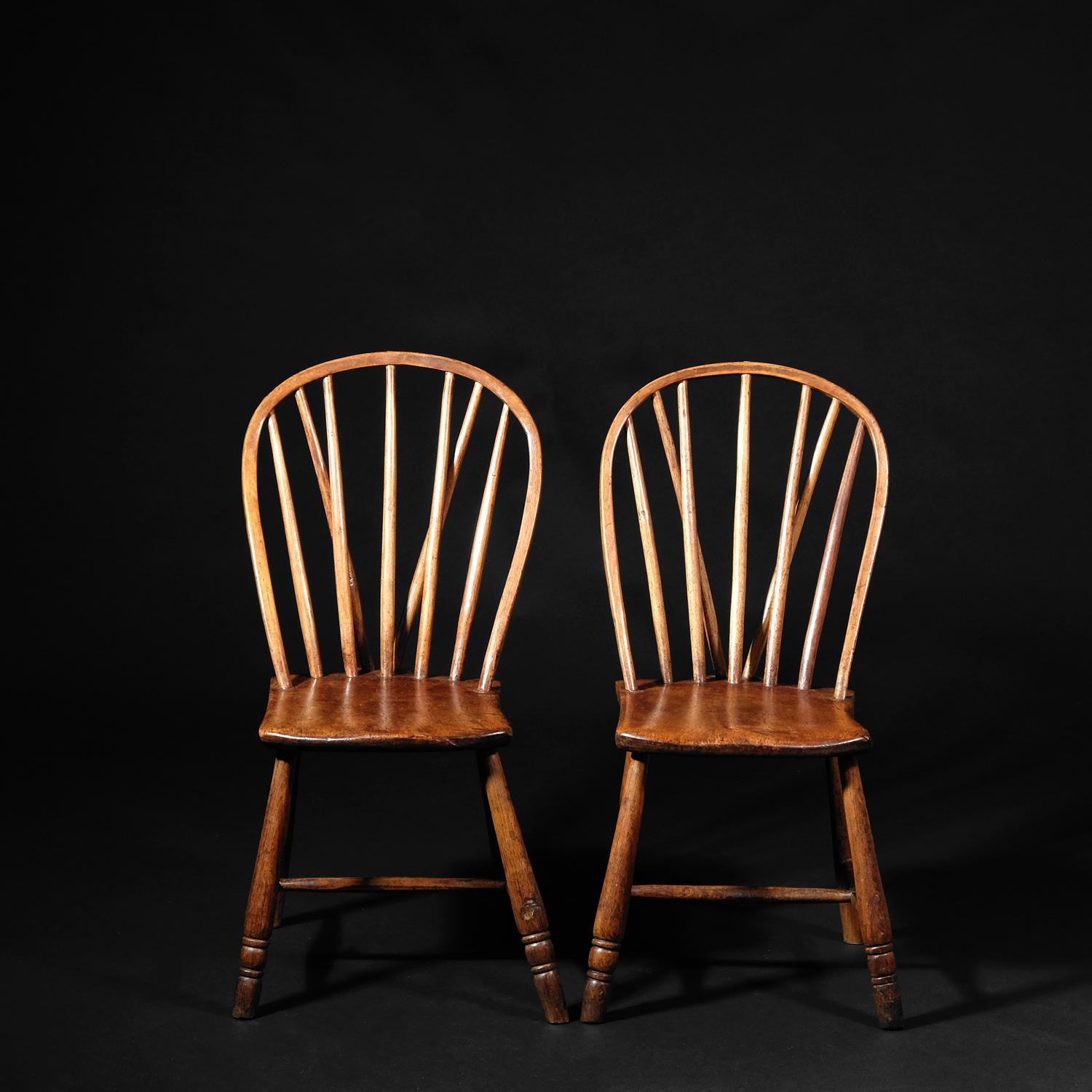 A matching pair of vernacular chairs in sycamore and ash. Egg and reel turned front legs with plain rear, united by a tapered H-stretcher. The shaped seats supporting a simple stick and hoop back. The 5 spindles, being hand-drawn and elliptical in