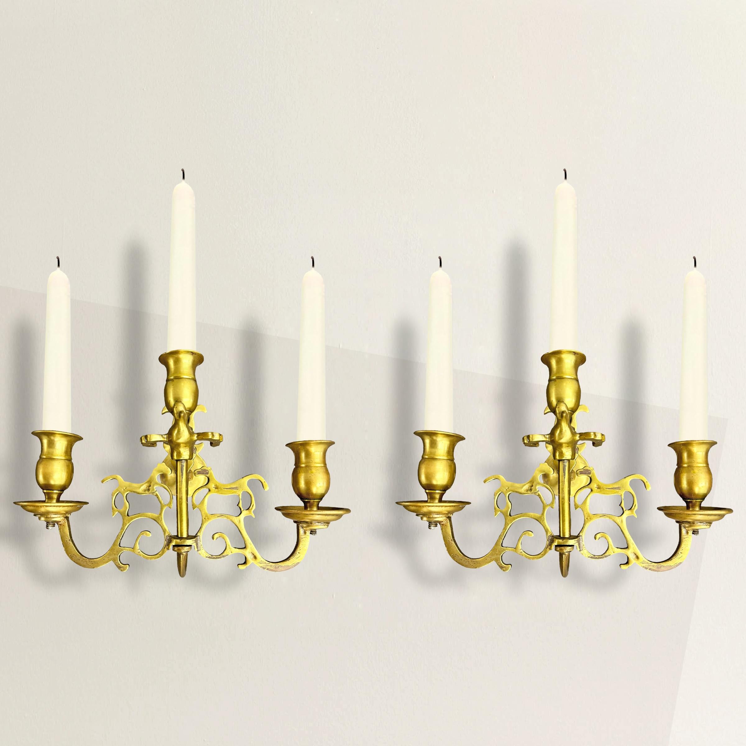 This exquisite pair of 18th-century English Georgian brass three-arm candle sconces embodies the elegance and ornamental richness of the Georgian period (1714-1830). Each sconce features a meticulously crafted pair of galloping horses facing each