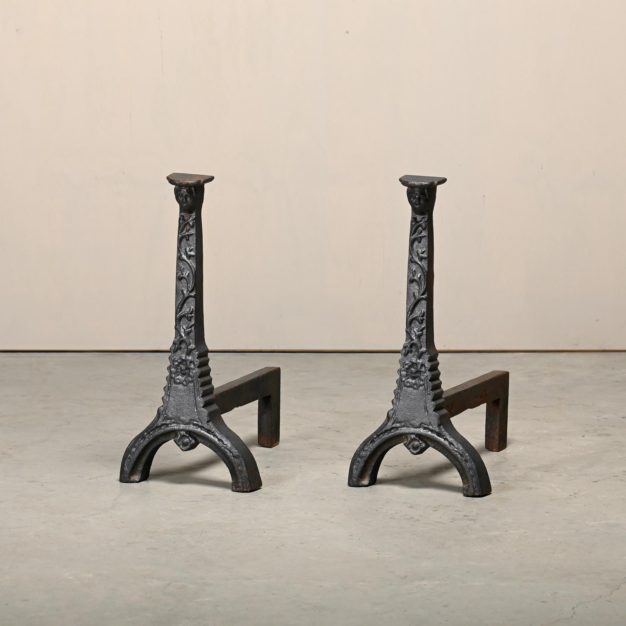 A pair of large antique 18th Century cast iron Firedogs / Andirons with flower motivs and finials in the form of faces wearing headdresses. Very good condition with minor wear. Sturdy and very heavy.