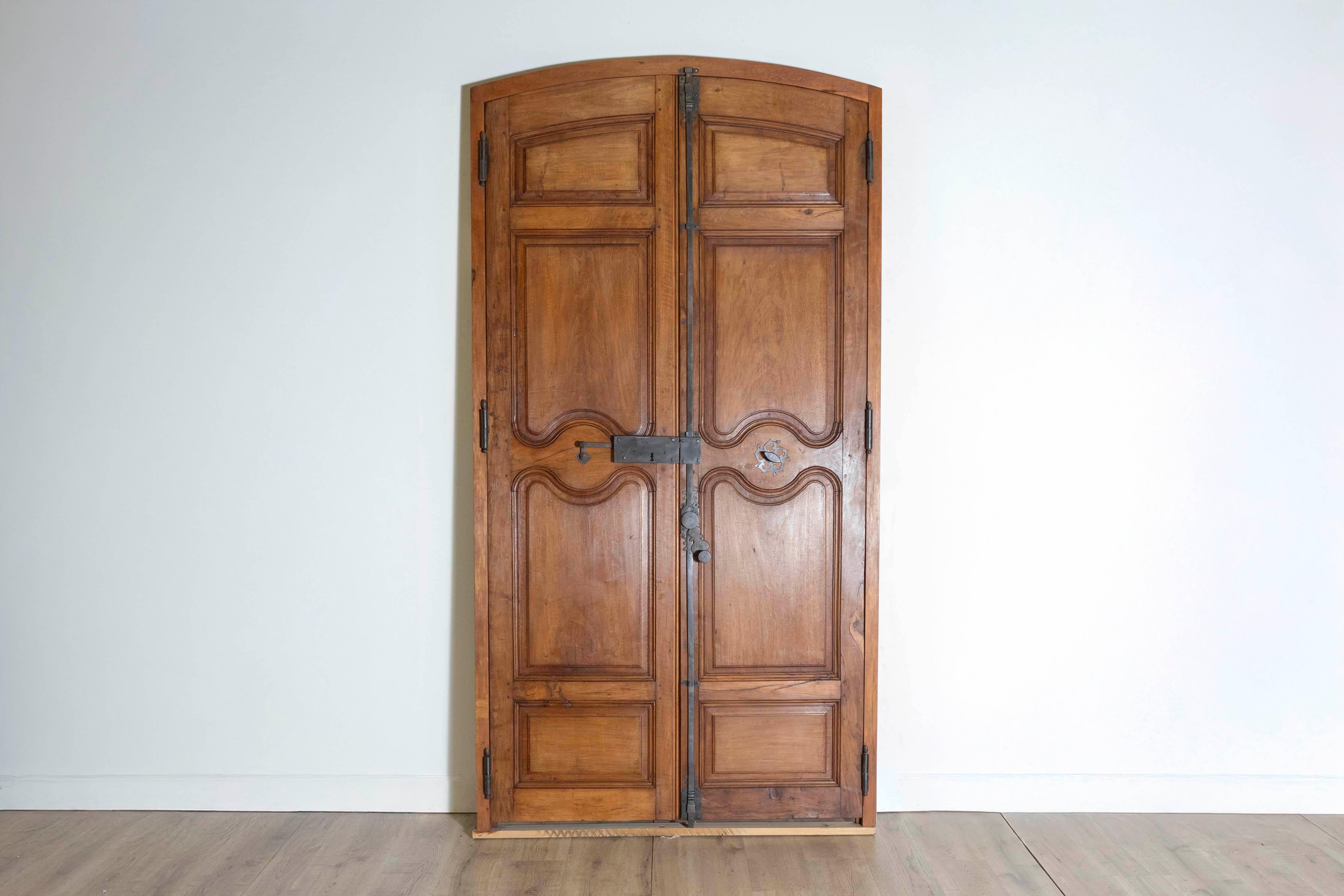This pair of 18th-century French communication doors displays an elegant blend of craftsmanship and rustic charm. Constructed from solid wood, likely walnut, they feature beautifully carved panels with intricate curved detailing in the central