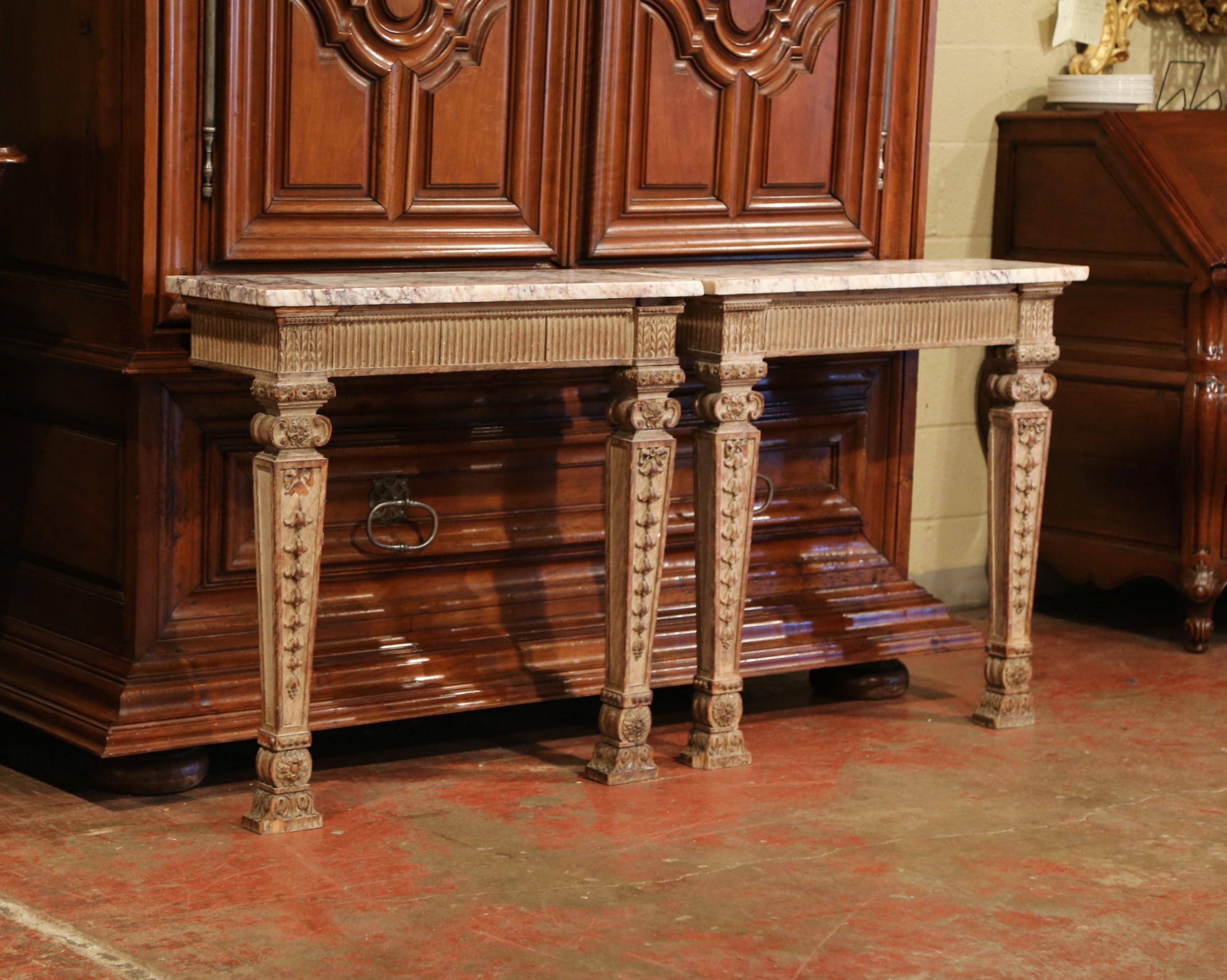 Decorate a hallway or bedroom with this elegant pair of antique, carved wall consoles. Crafted in France, circa 1760, each embellished table features heavy hand carved tapered legs and a central apron. The tables are topped with a white marble slab