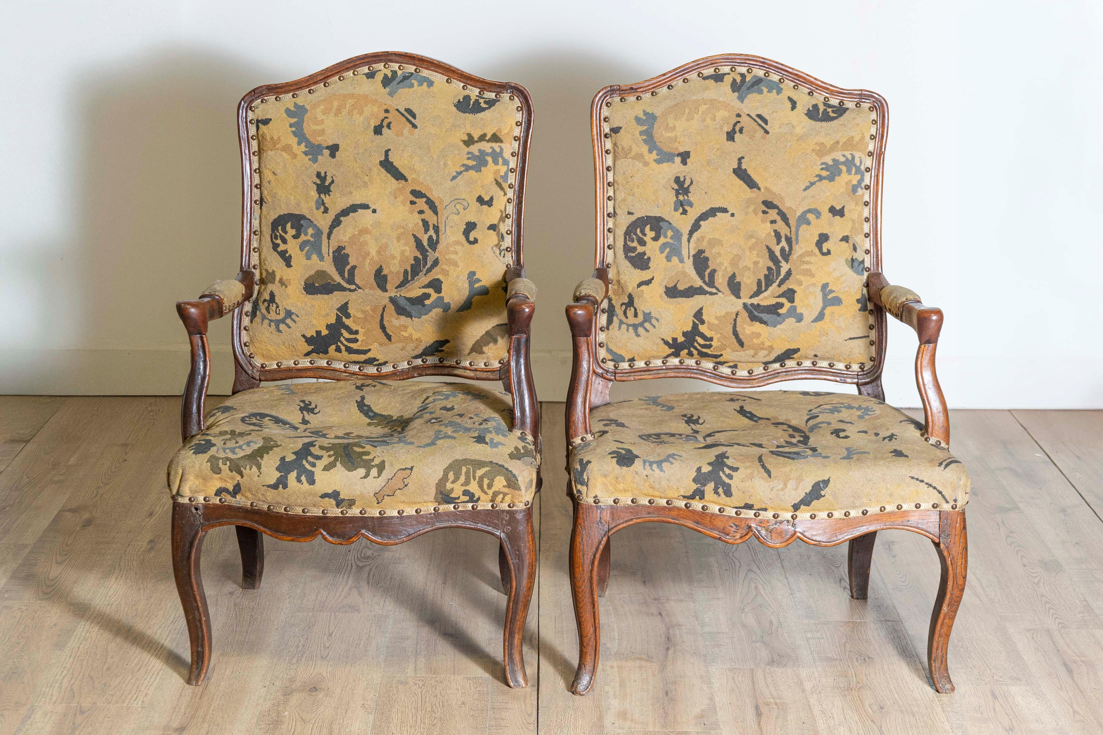 Cette paire de fauteuils Louis XV français du XVIIIe siècle illustre l'élégance gracieuse et le savoir-faire de la période Louis XV. Fabriqués en noyer, les cadres présentent de magnifiques détails sculptés à la main, notamment un tablier festonné,