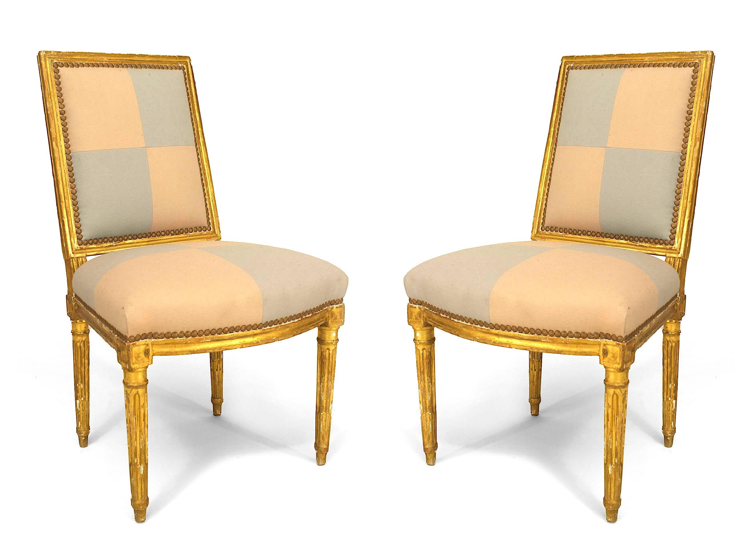 Pair of French Louis XVI (18th Cent) gilt side chairs with square back and upholstered in beige and blue square pattern on seat and back.
