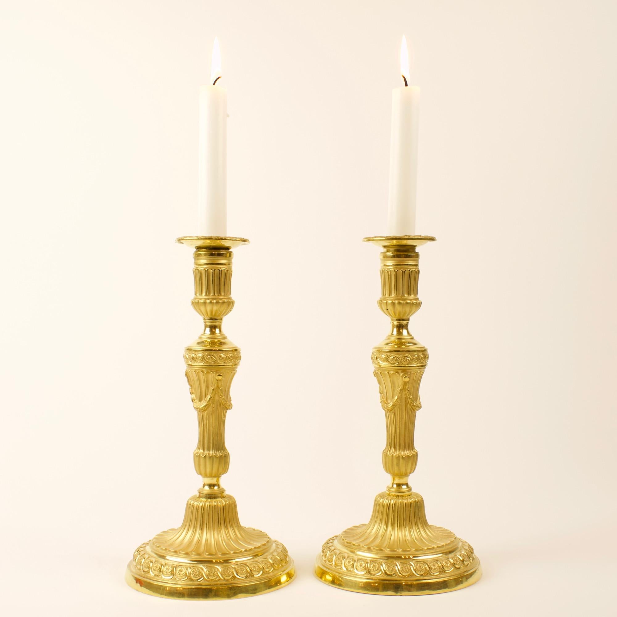 Large pair of 18th century French Louis XVI neoclassical gilt bronze candlesticks.

A fine pair of large Louis XVI period gilt bronze candle sticks, each with a fluted tapering stem and fluted plinth and nozzle, base and upper rim of the stem cast