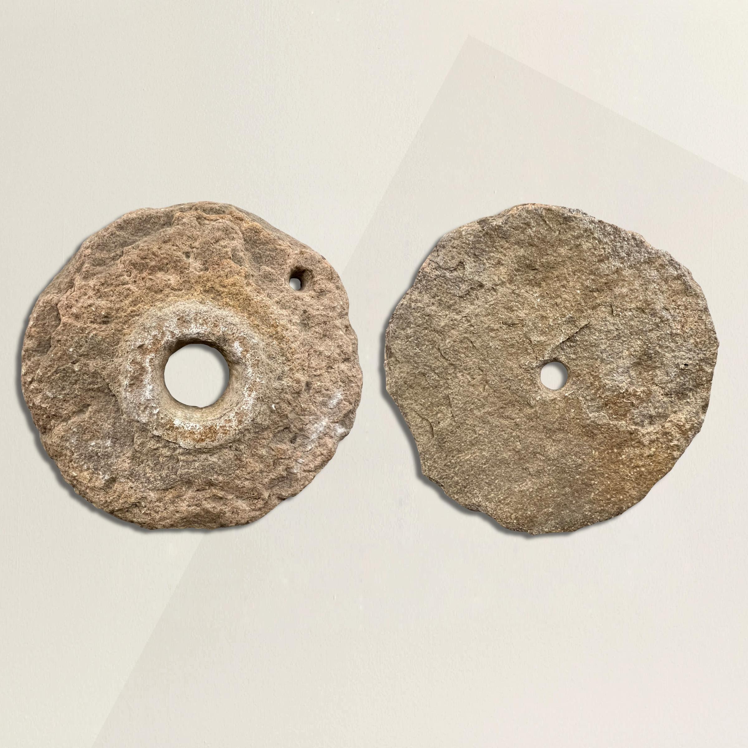 A stunning pair of 18th century French millstones carved from pink granite and each with a rough, well-worn surface, originally used to crush course grains. We've mounted each stone on custom steel wall mounts so they can be arranged in any way to