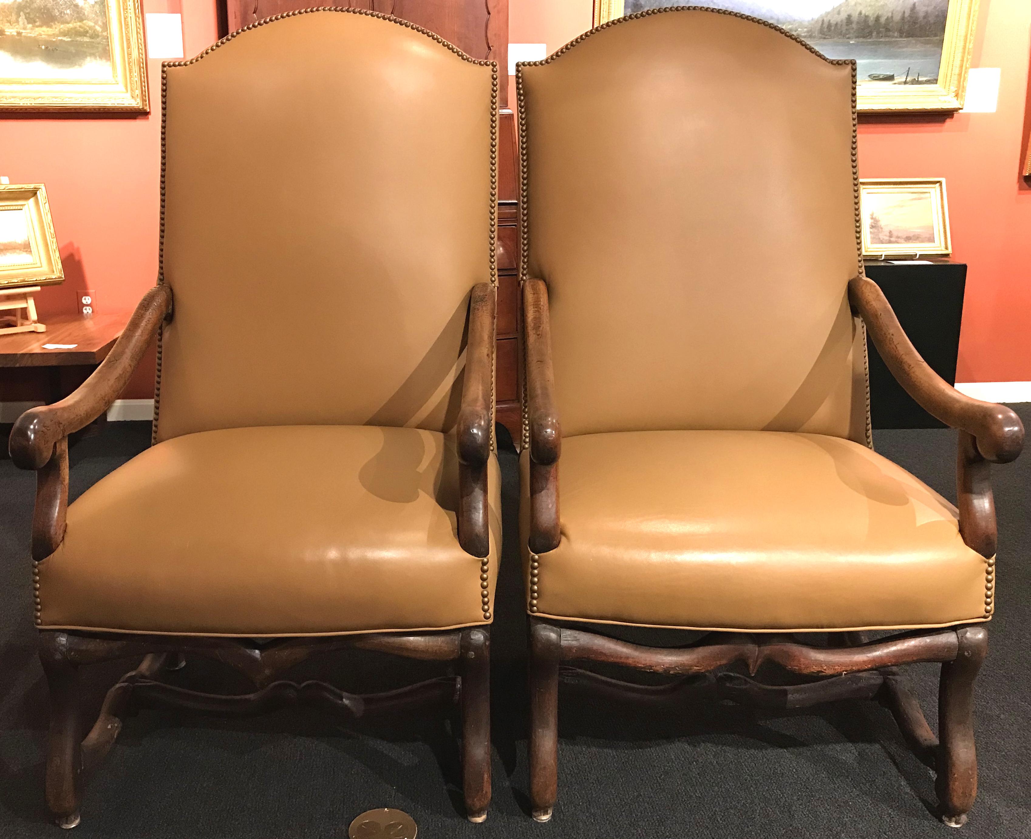 A fine pair of 18th century French walnut armchairs with chapeau de gendarme form backs, H-shaped os du mouton carved stretchers, and recent tan leather upholstery with nailwork border. Pegged construction and great overall patina, with some old