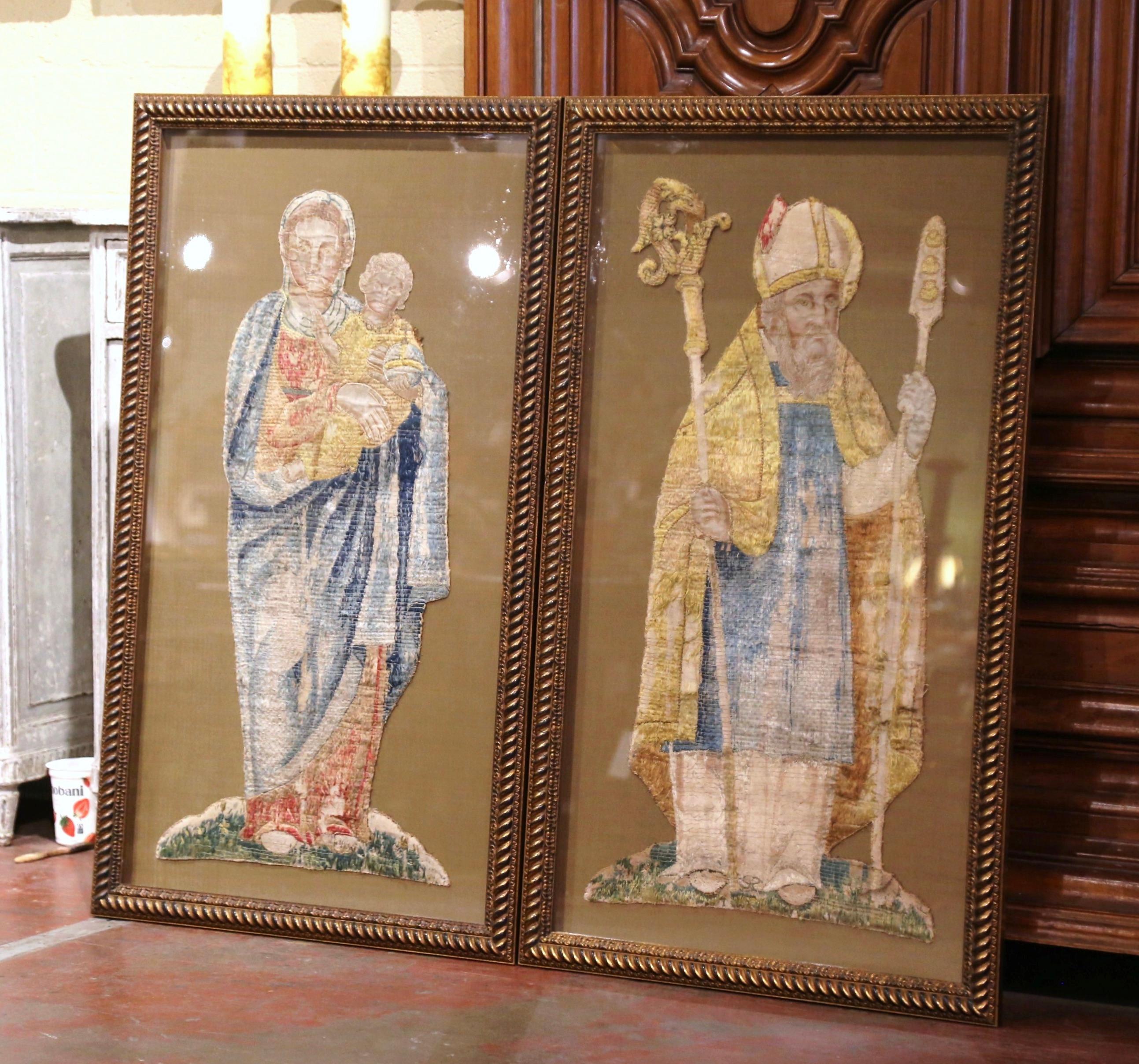 Decorate a study or hallway with this large and colorful pair of wall decor. Set a carved giltwood frame protected with glass, each panel depicts a religious figure including the Virgin Mary holding her Son Jesus Christ. The other represents a