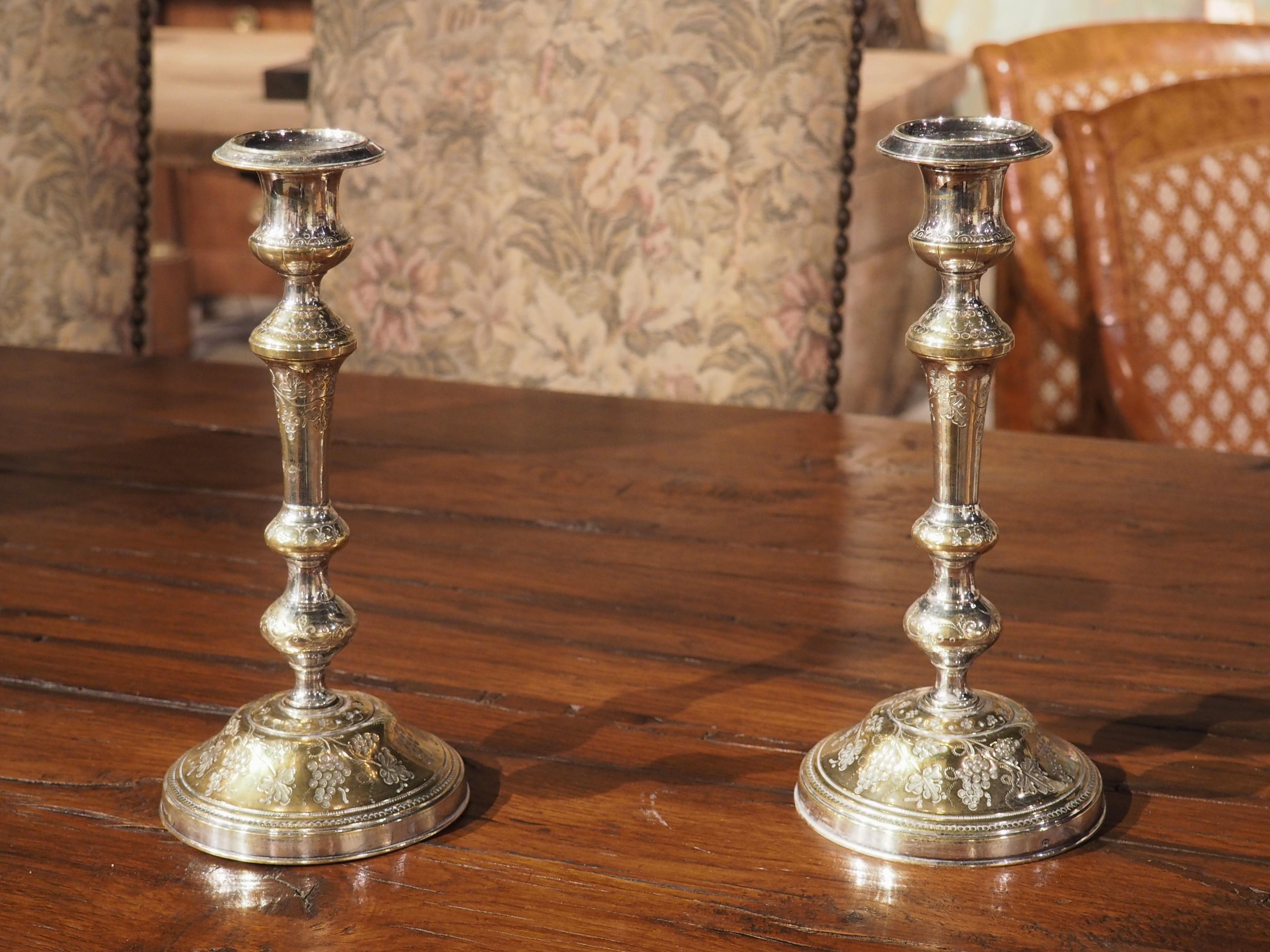 Cast in France during the 1700s, this pair of silvered bronze candlesticks has been delicately chased with grape cluster designs. The highly sinuous candlesticks feature several knops, all adorned with a variety of grape motifs. Additional elements
