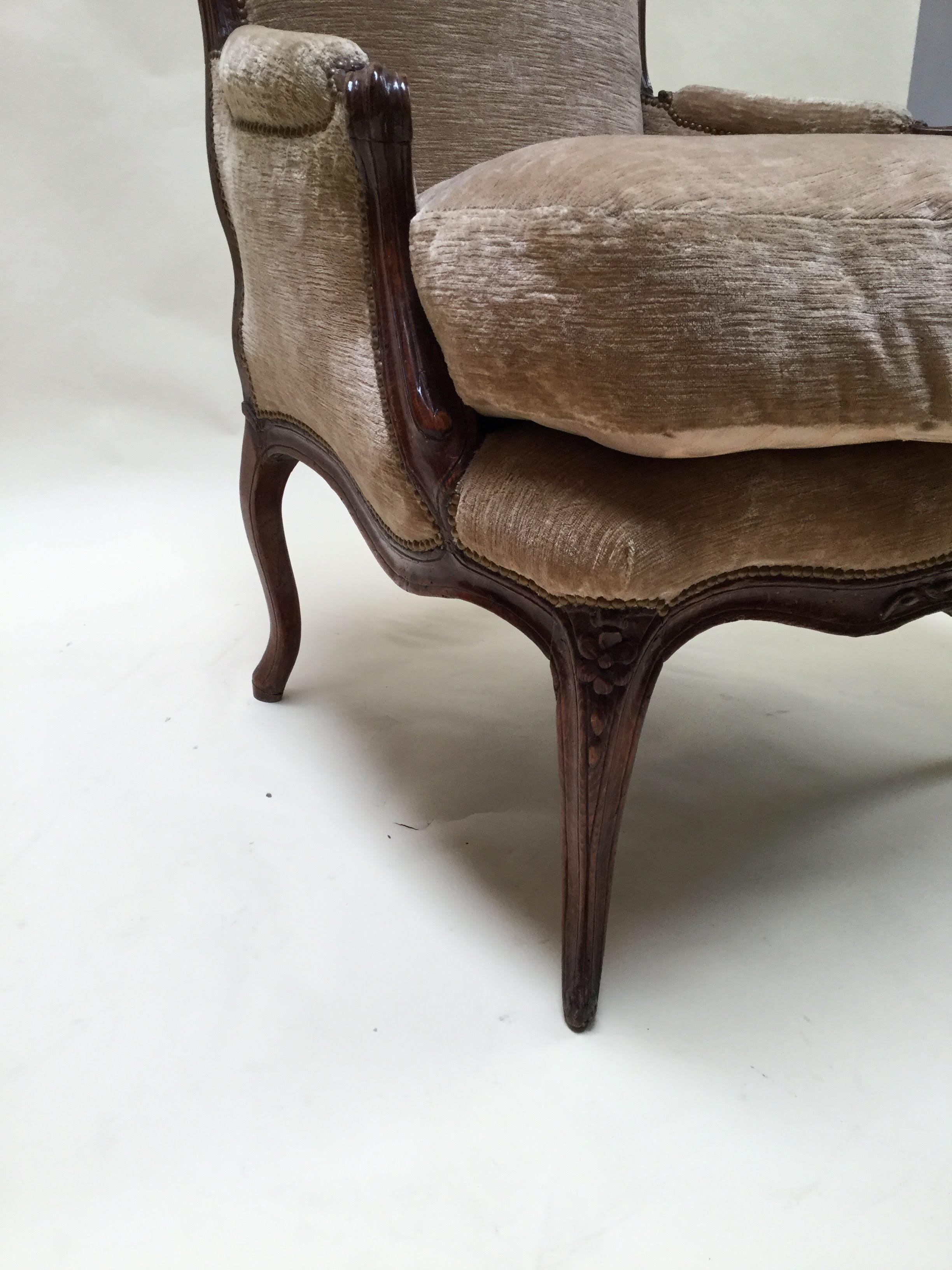 Masterfully crafted pair of Bergere chairs, resting on curved carved legs and curved back with central flower medallion detailed repeated on front rail. Frames and velvet upholstery is in great condition.