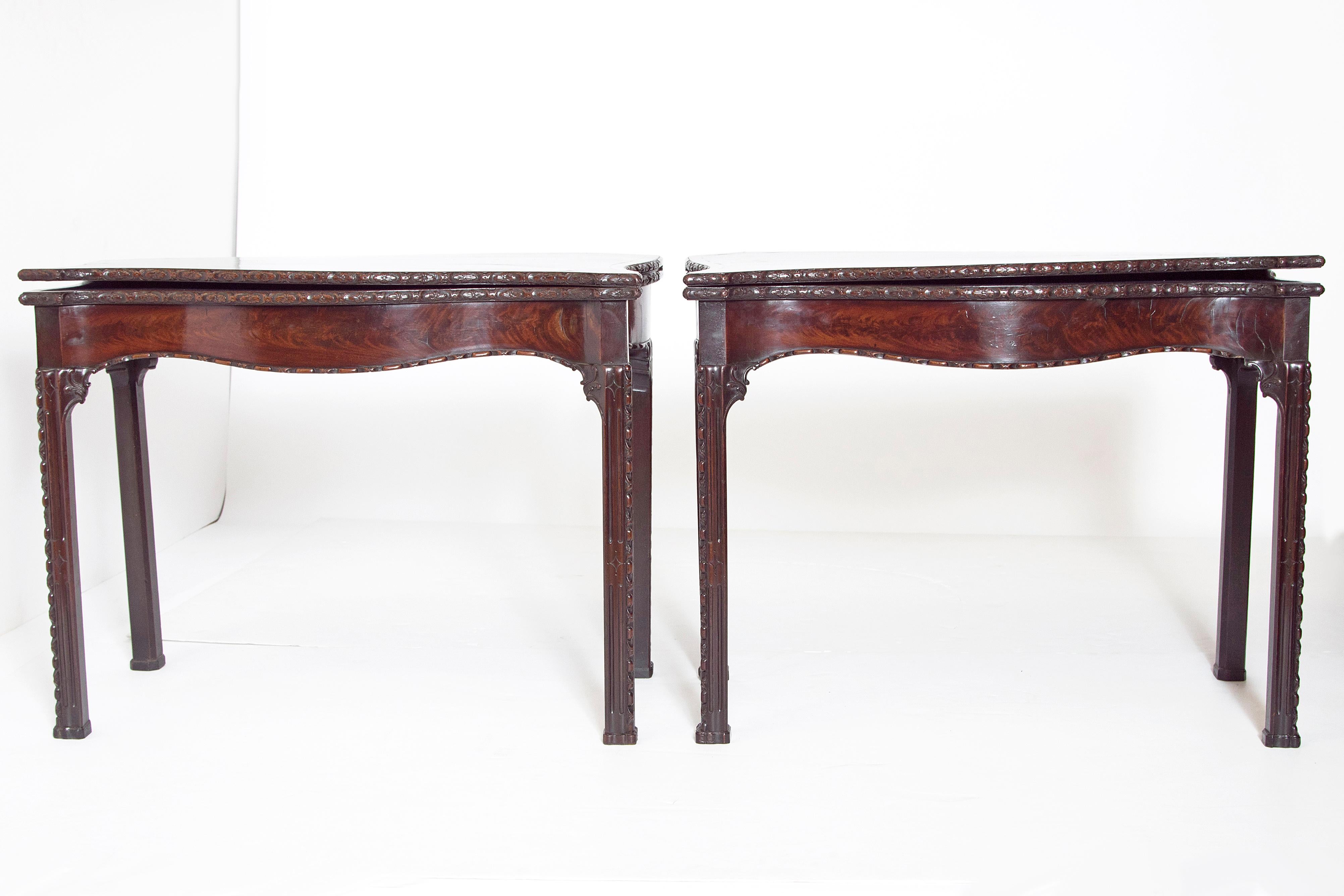 A pair of early George III flip topcard tables with blue baize lining. The tables feature a unique serpentine front and sides. The top edge has a carved floral decoration with well figured mahogany and an inlay border. A carved decoration continues