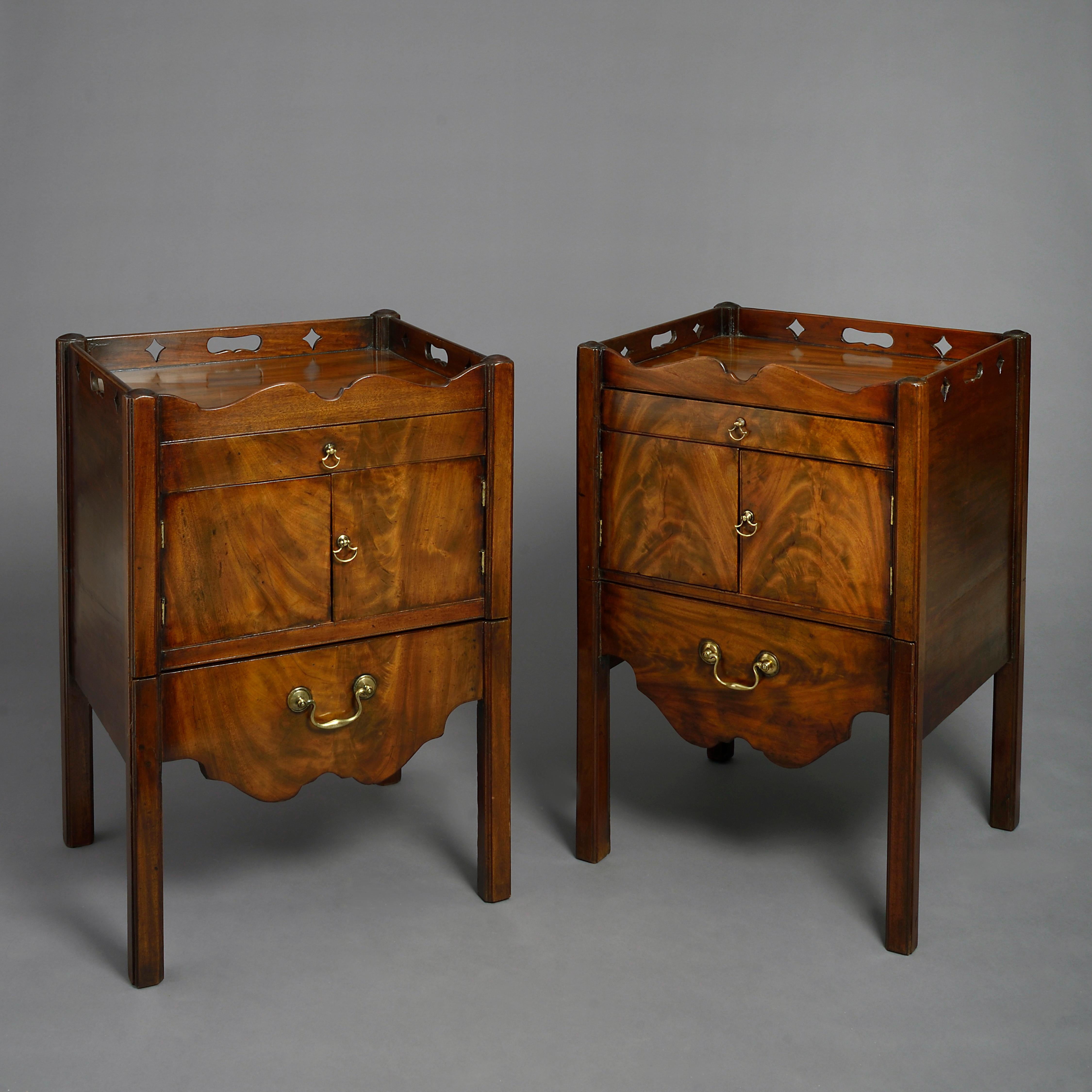 A fine pair of mid-18th century George III Period mahogany bedside cupboards of good color and figuring, each supporting a galleried top with pierced carrying handles above a drawer, two cupboard doors and a lower slide with shaped apron, suede