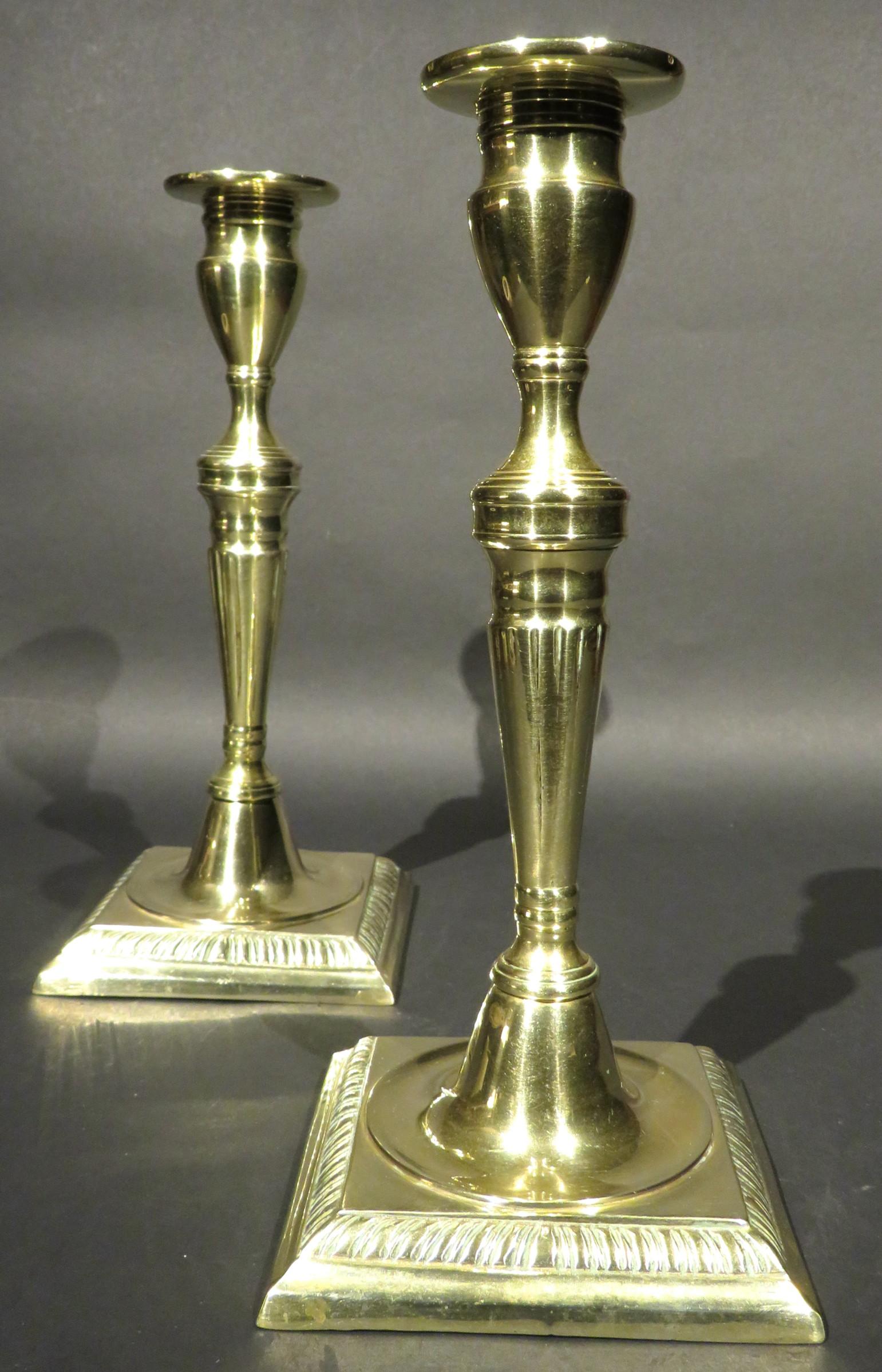 A very good pair of 18th century George III brass candlesticks, both showing fluted tapering columns rising to tulip shaped nozzles with flattened drip pans, raised on squared bases with chiseled gadroon detail. Both exhibiting a fine patina and an