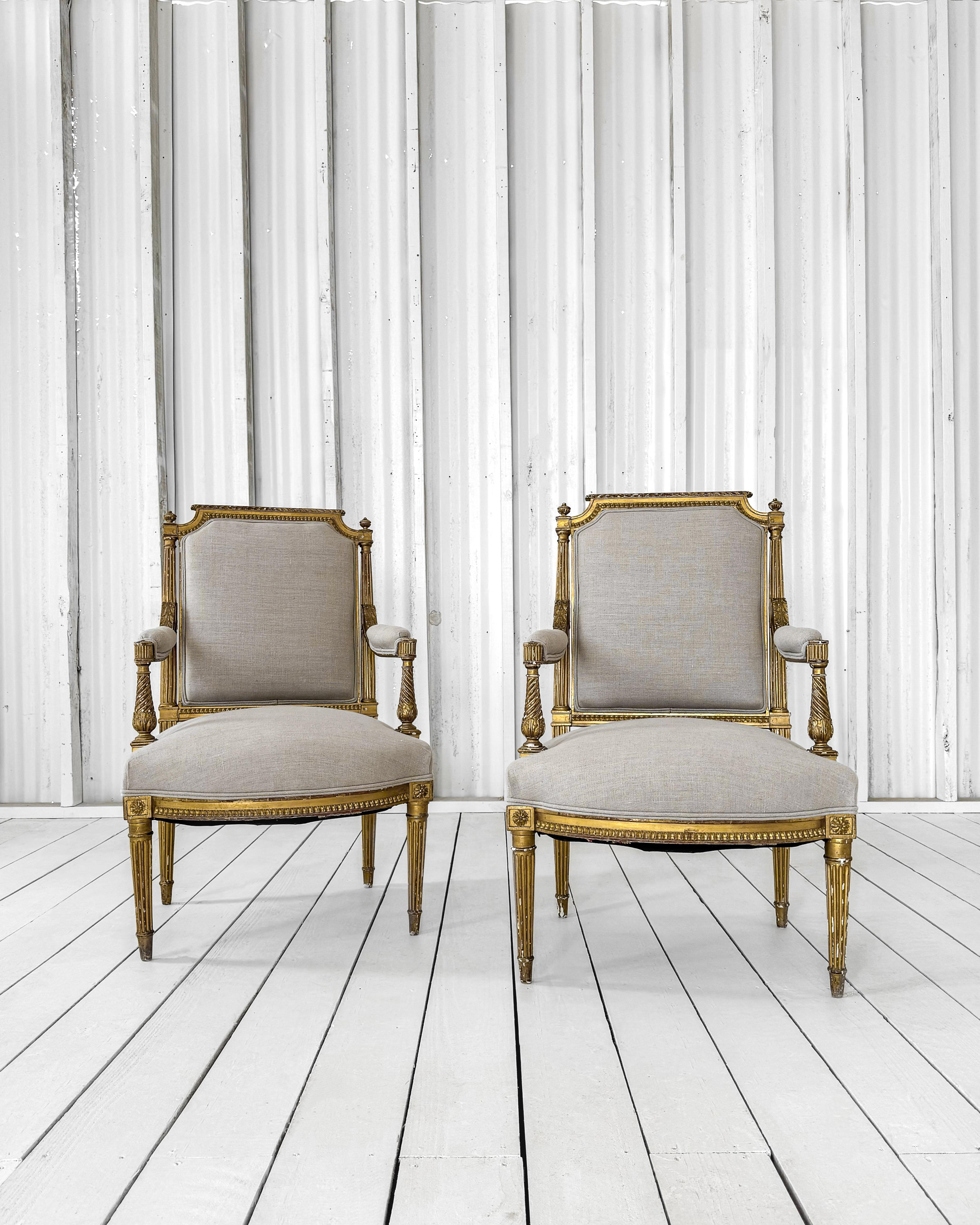 Beautiful antique Louis XVI fauteuil armchairs featuring a hand-molded frame and square-shaped back. Crafted from solid wood using mortise and tenon construction, the fluted outer back of the chair’s frame is adorned with ornate detailing along the