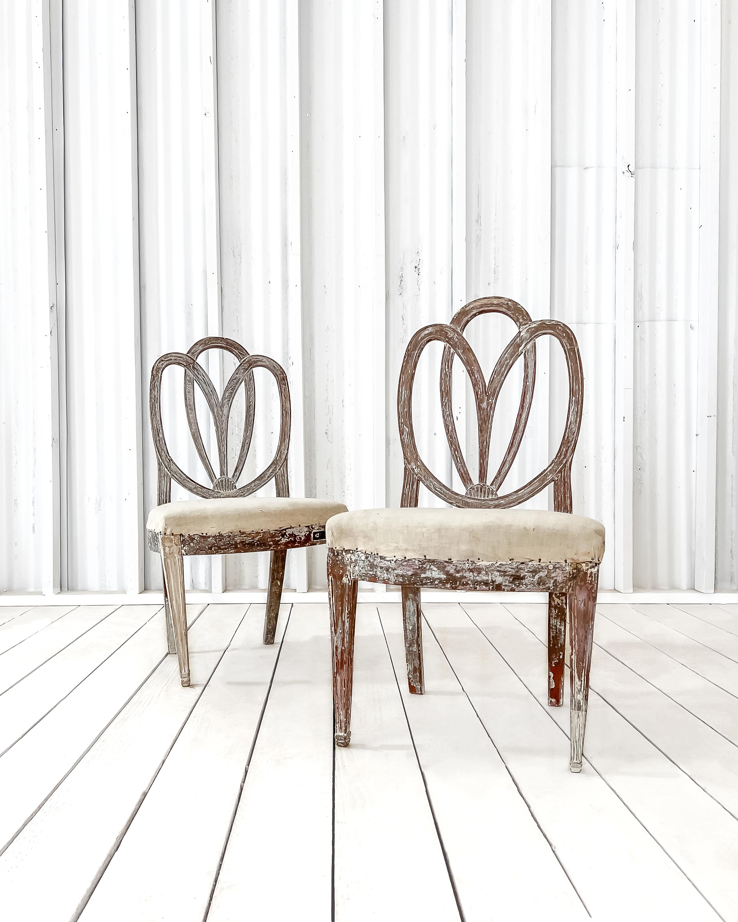 A pair of Swedish Gustavian period side chairs. Crafted from solid wood during the late 18th century, these beautiful chairs feature hand-carved detailing and gracefully curved tulip backs. The body of the chairs has been dry scraped, revealing