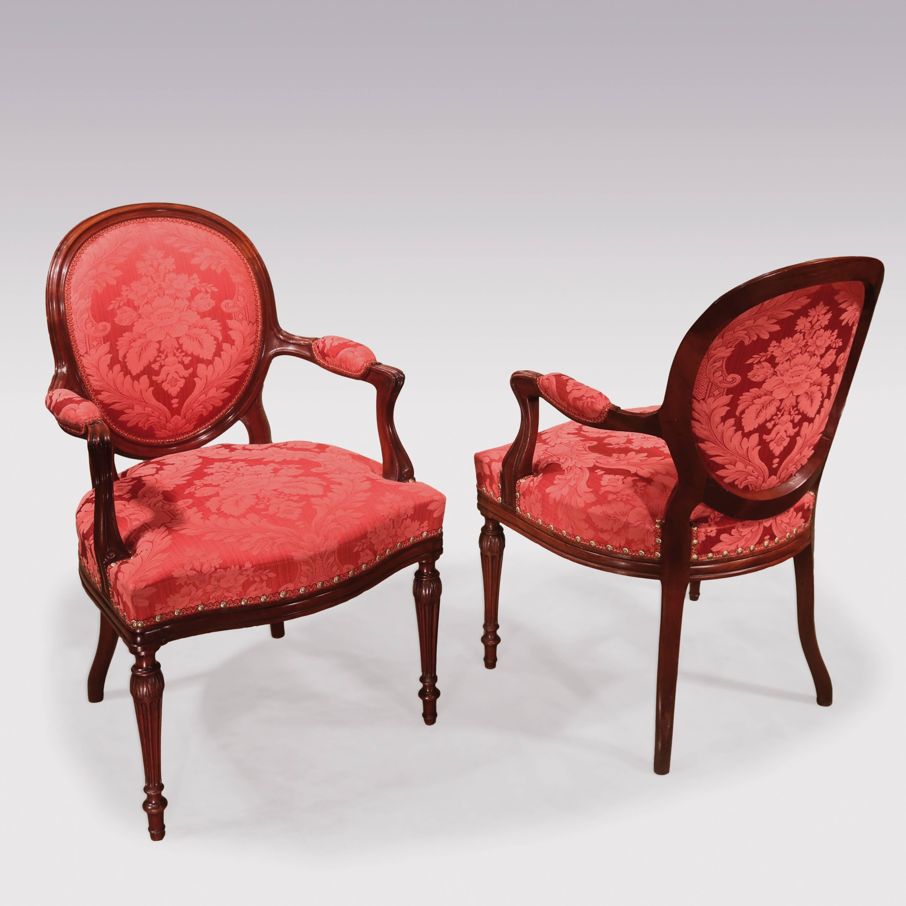 A pair of late 18th century Hepplewhite period mahogany armchairs, having moulded show-wood oval backs with scrolled set-back arms, above stuff over seats with moulded border, supported on acanthus carved turned, fluted tapering legs.