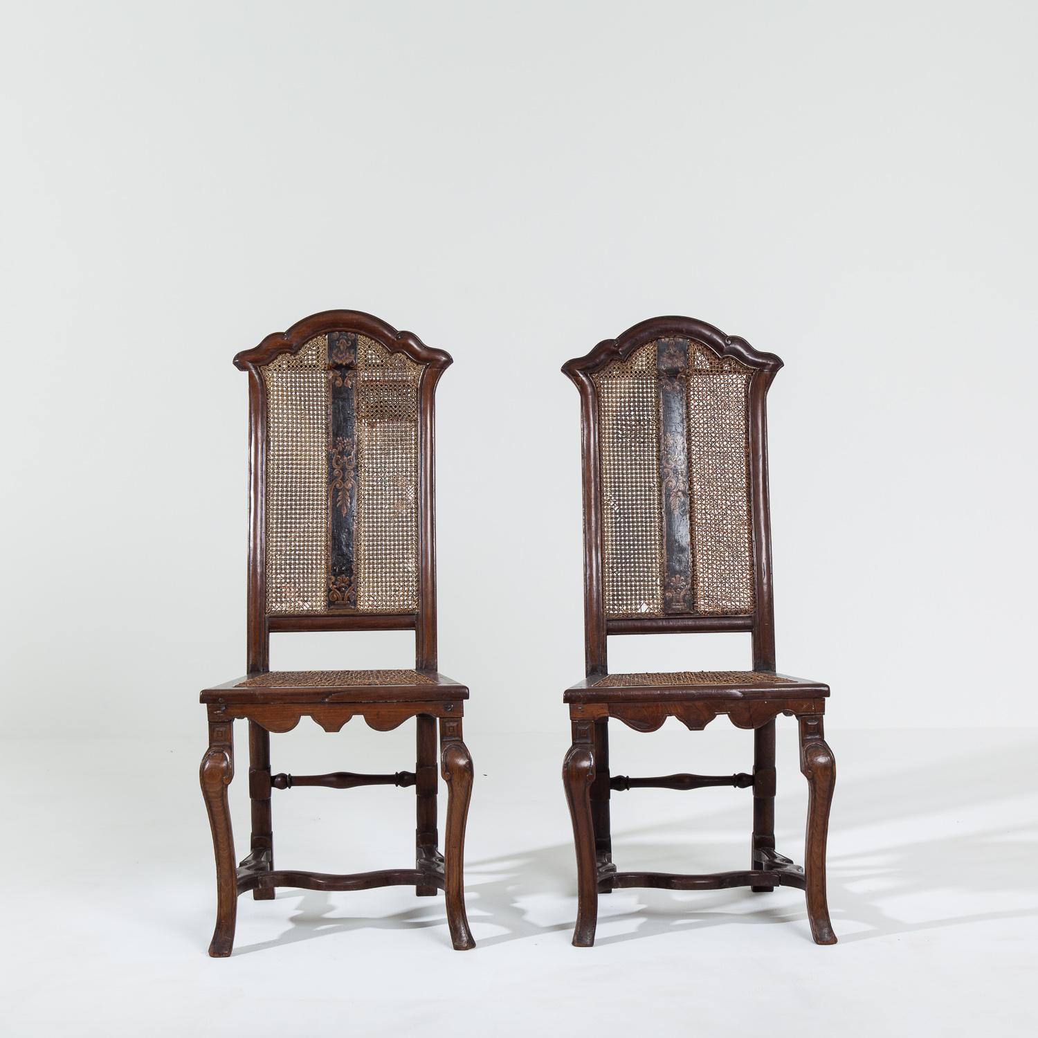 Pair of Italian walnut side chairs featuring a decorative painted panel.

The chairs have caned seats and backs, showing signs of repair work and some minor breakages. Historic repair patch to the back of one of the chairs.

Measure: Height 107cm x