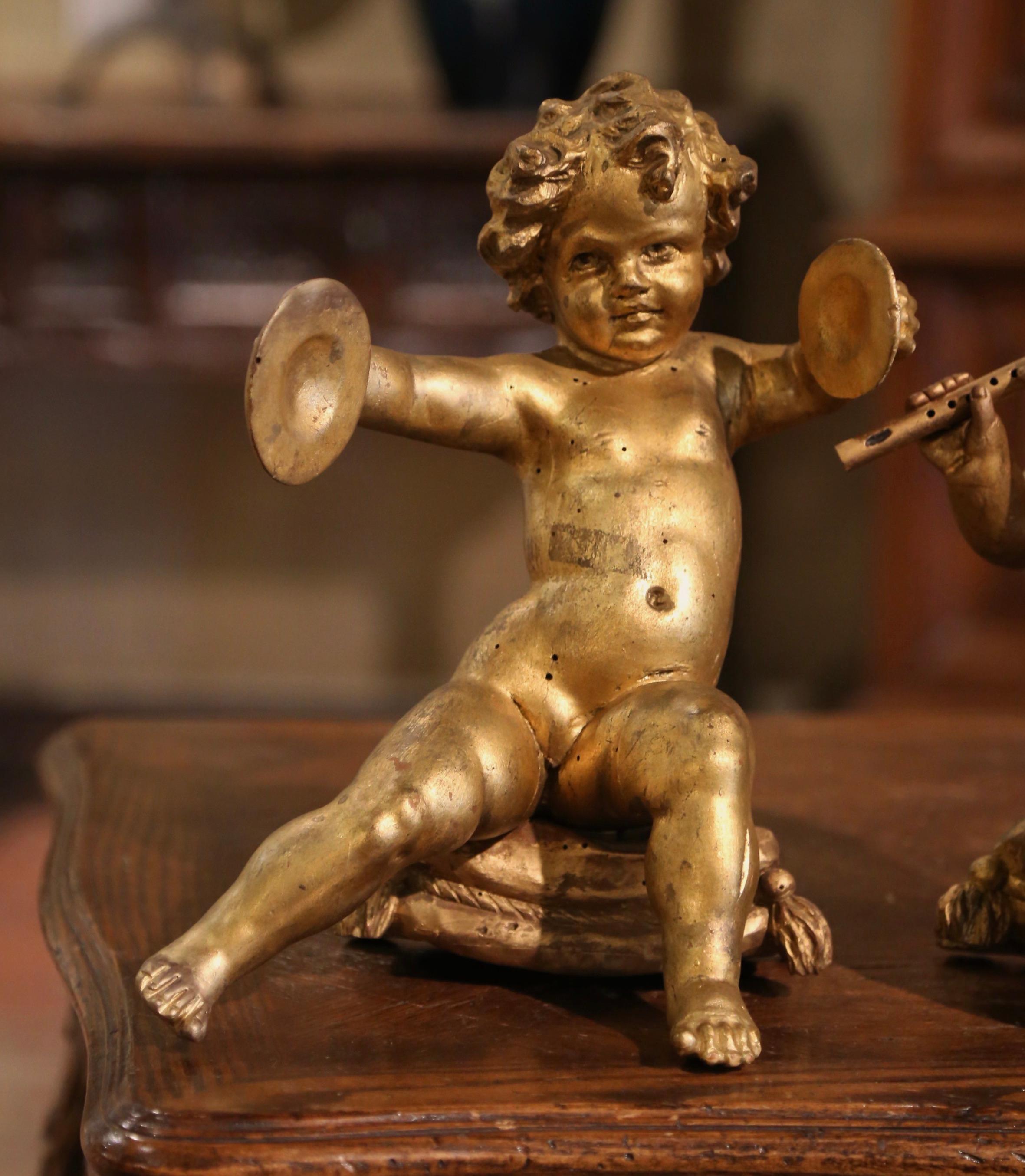 These charming antique putti carvings were crafted in Italy, circa 1780. The hand carved figures depict two musicians cupids sited on a pillow form stool; one playing the flute, the other holding cymbals. Each sculpture features its original gold