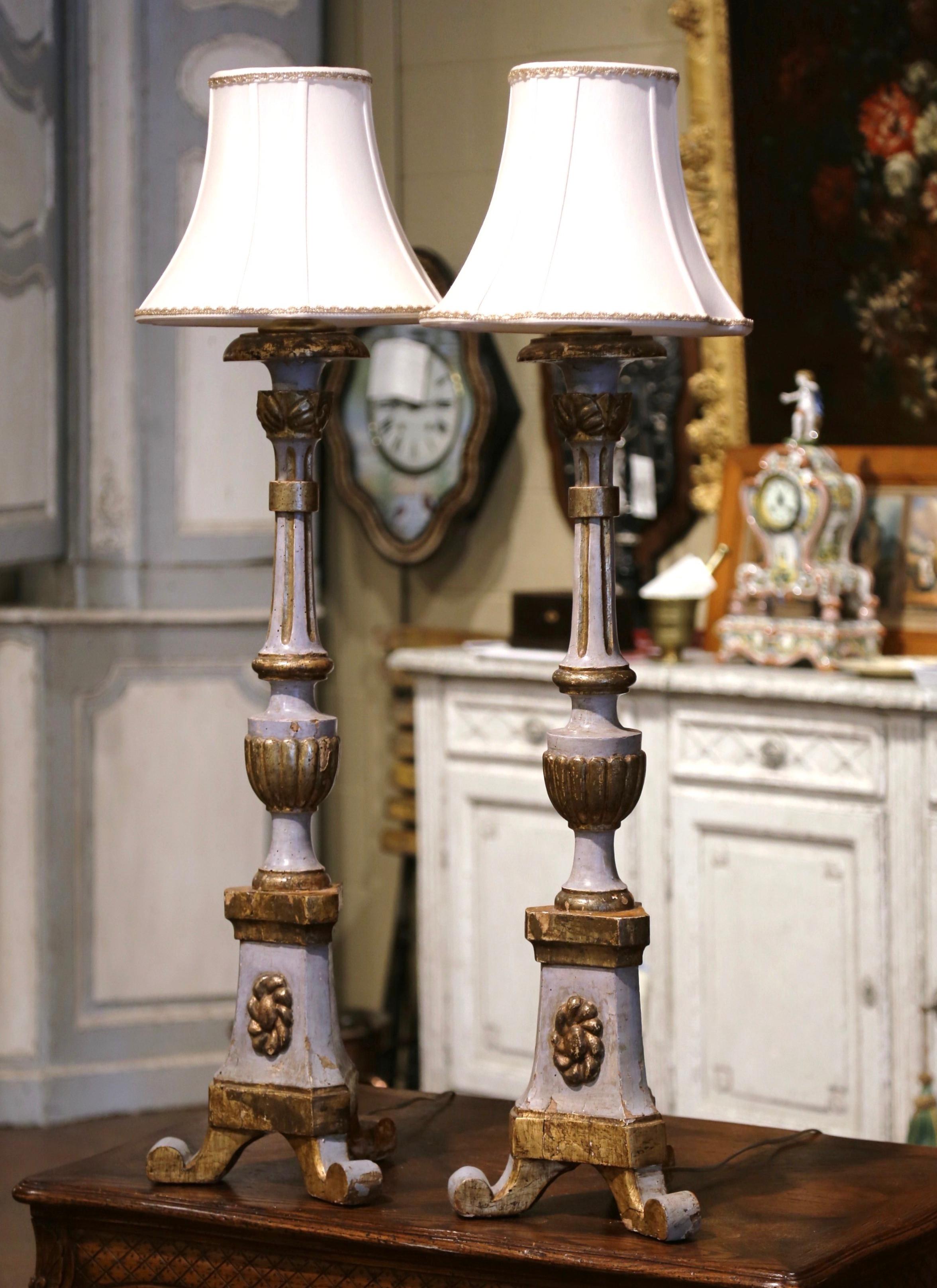 Add an air of drama and elegance to your home with this pair of antique table lamps. Crafted in Italy circa 1760 and converted into table lamp, each candlestick stands on a tripod base decorated with a carved floral medallion, and ending with