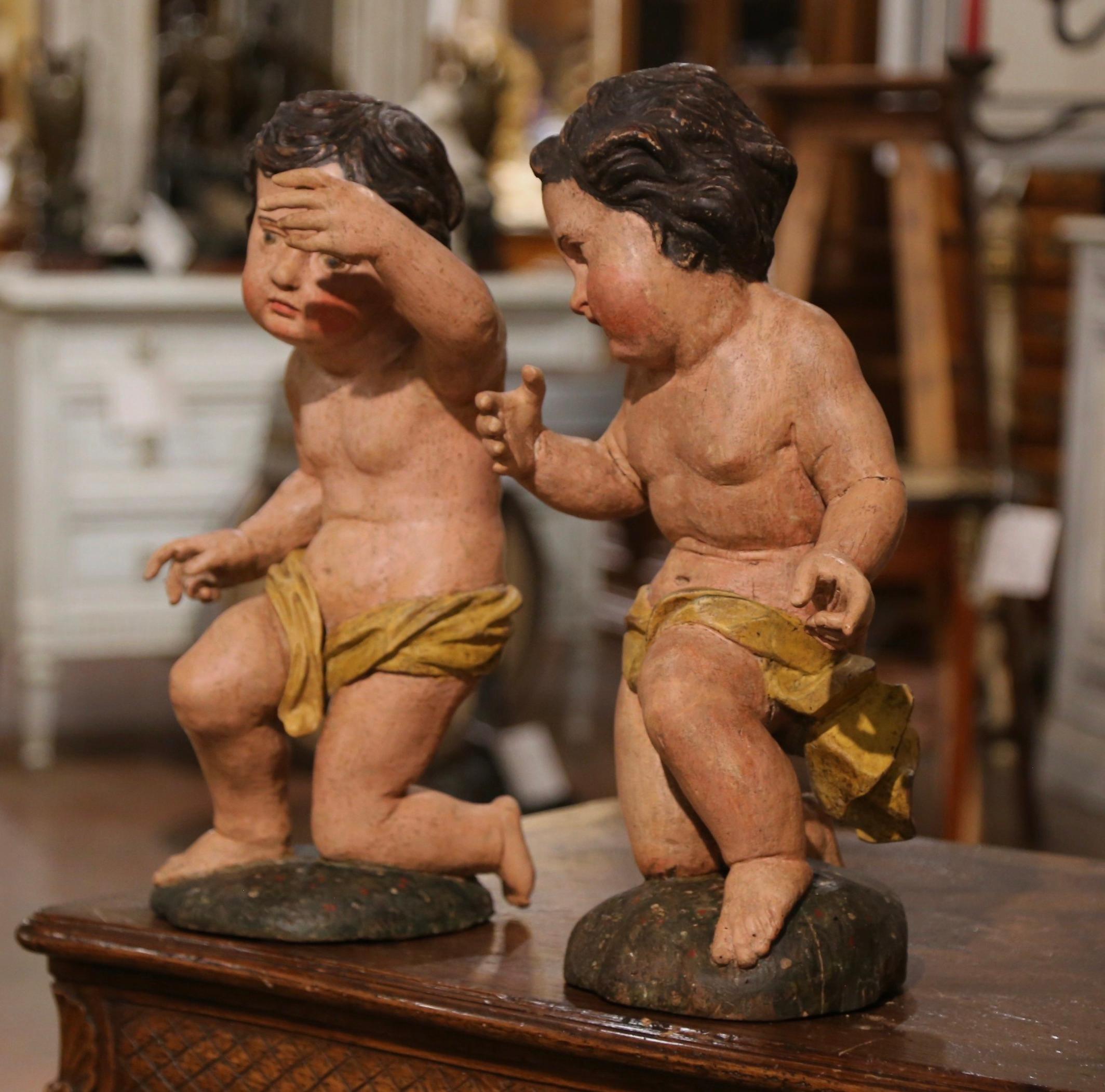 These charming antique putti carvings were crafted in Italy, circa 1780. The hand carved figures depict two chubby cupids resting on a knee and holding a arm up; each sculpture features its original polychrome and gold leaf finish for a luxurious