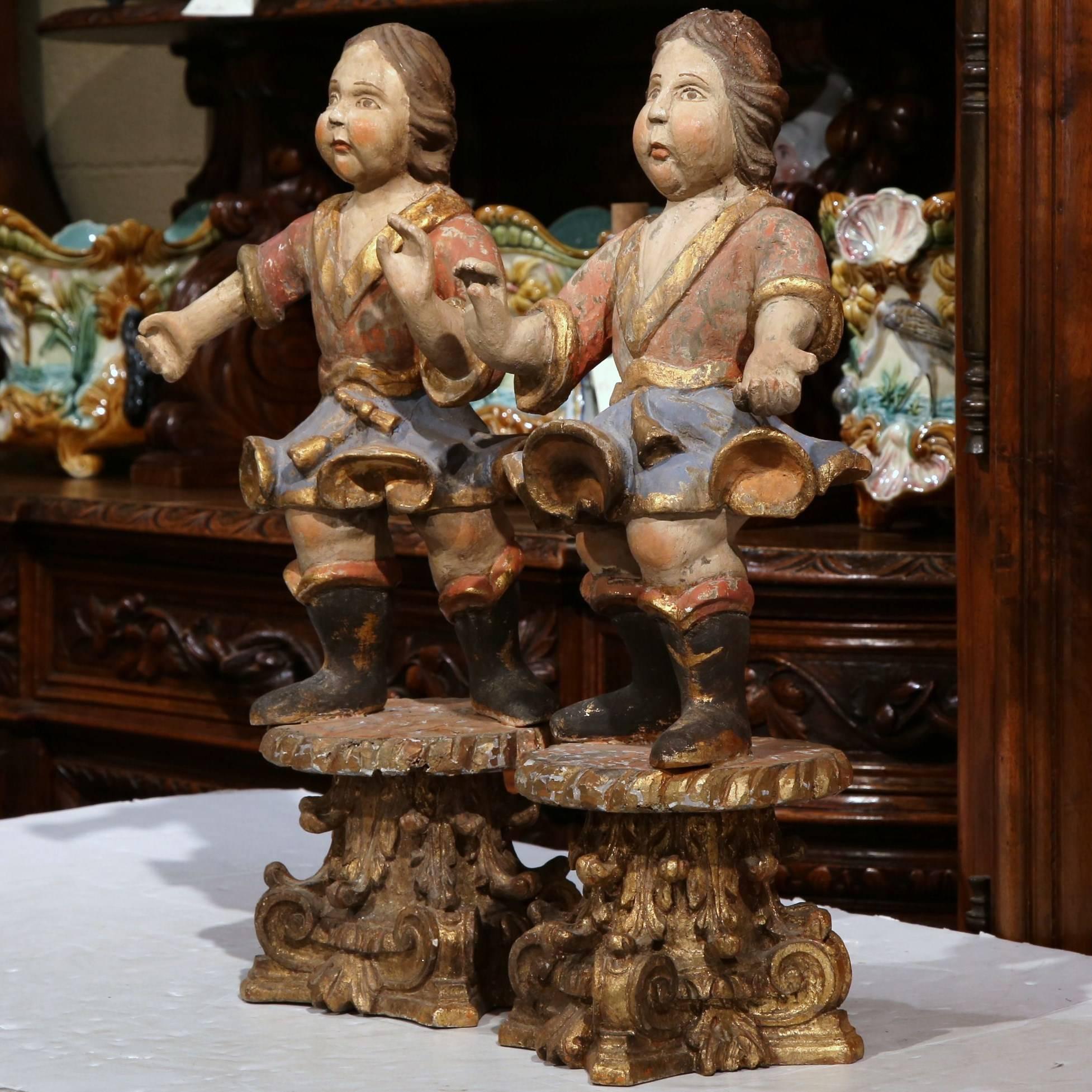 Place this beautiful pair of antique carved figurines on a mantel or a console. Crafted in Italy, circa 1780, the tall sculptures depict two chubby cherubs standing on carved gilt bases decorated with acanthus leaves. Both hand carved sculptures