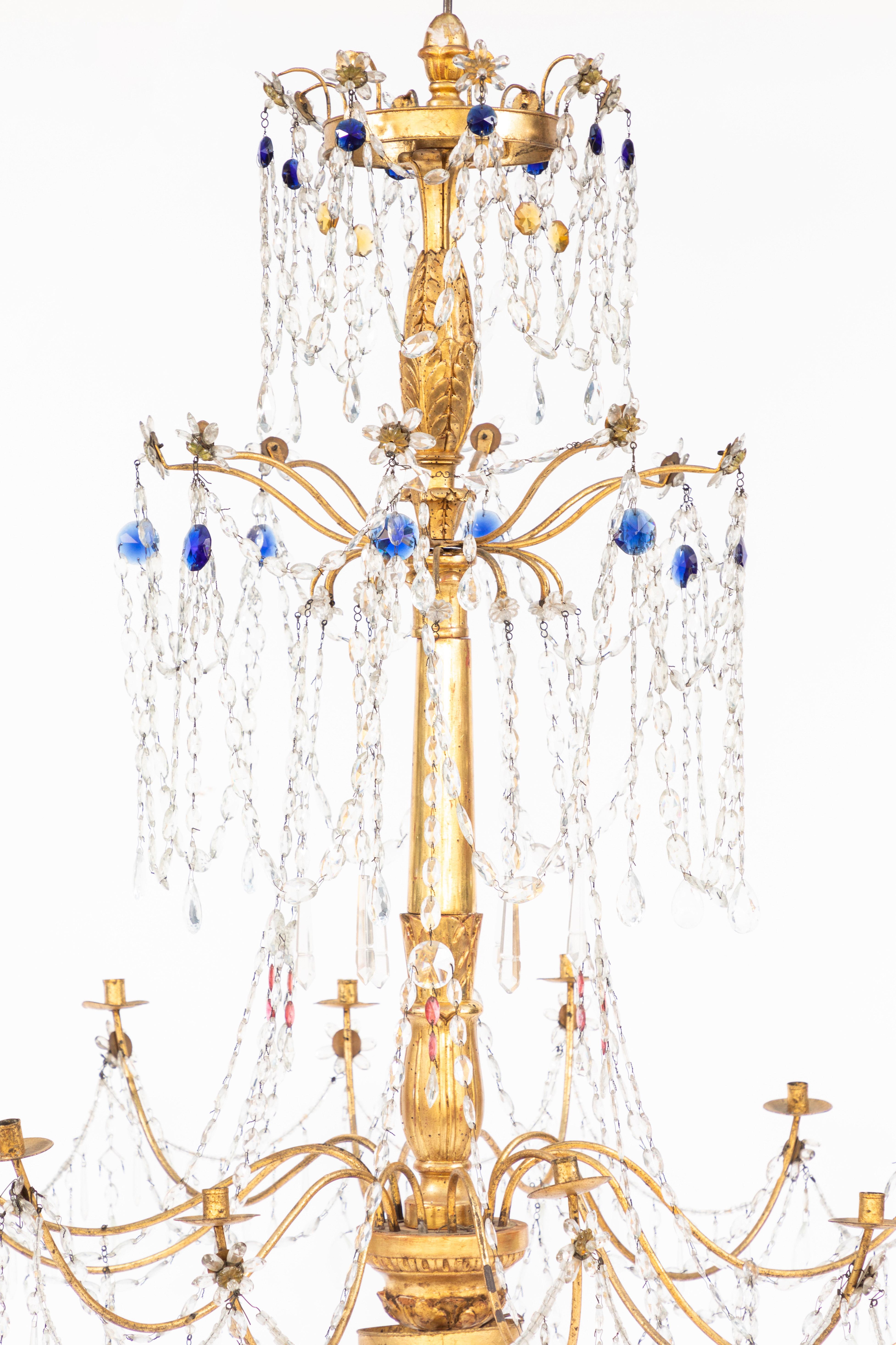 Pair of 18th century Italian giltwood and gilded iron chandeliers with sapphire and ruby colored crystals. All hand knotted. They are candle chandeliers but can be electrified.