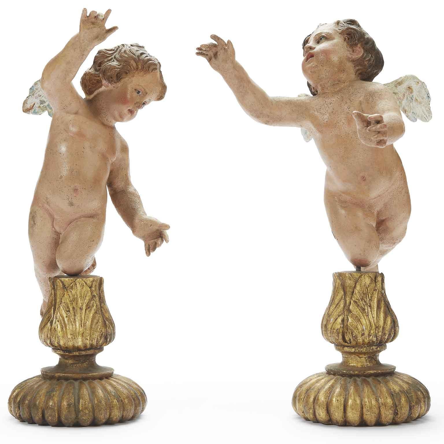 A stunning pair of Italian Baroque polychrome earthenware winged putti figures with glass eyes,  dating back to the early 18th century, Neapolitan origin, standing on later circular carved giltwood bases in good age related condition, with minor