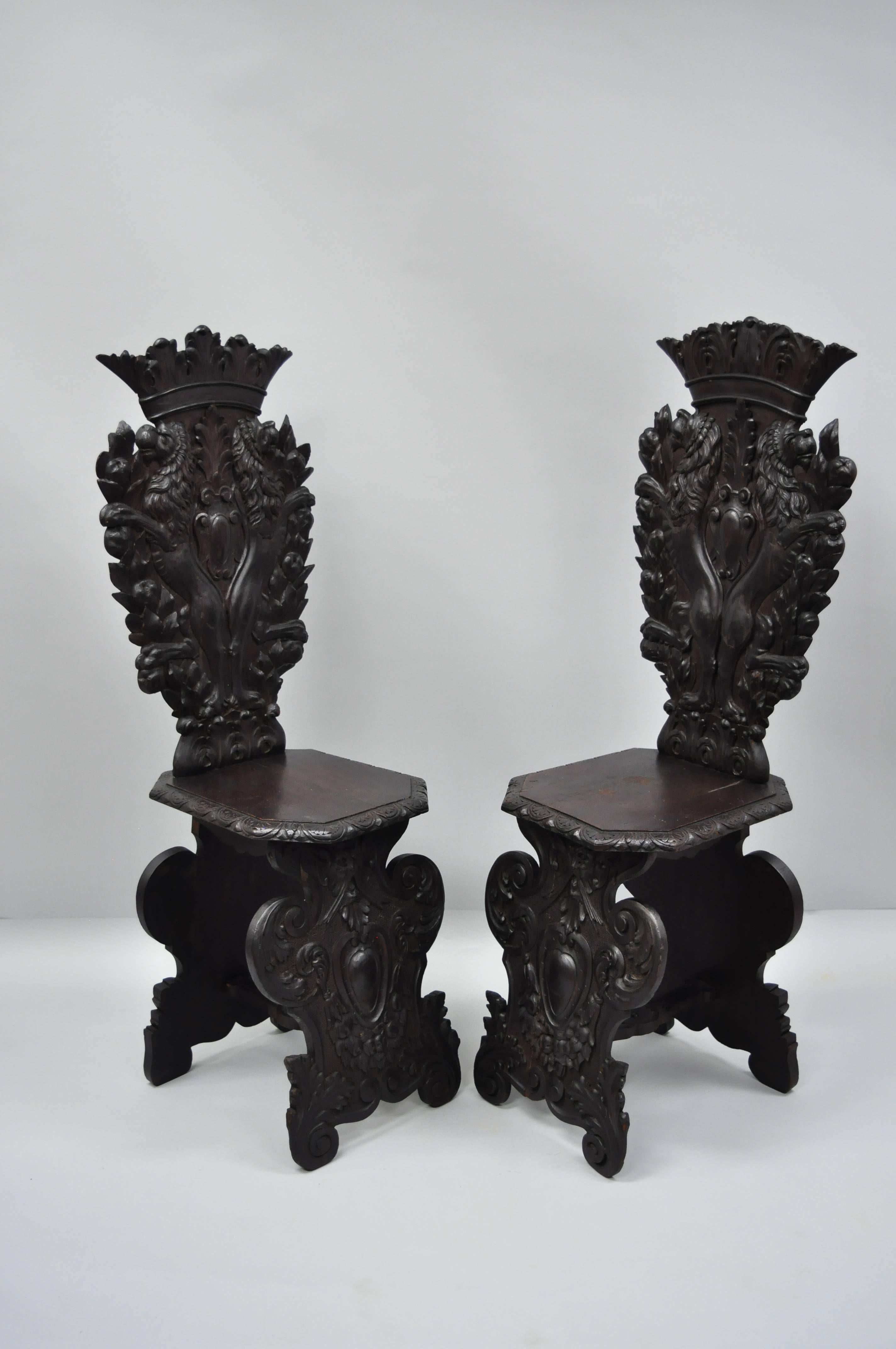Paire de chaises de salle Sgabello en noyer sculpté au lion, de style Renaissance italienne du XVIIIe siècle. L'objet est fabriqué en bois massif et présente des détails finement sculptés de lions, de couronnes royales et de rinceaux d'acanthe