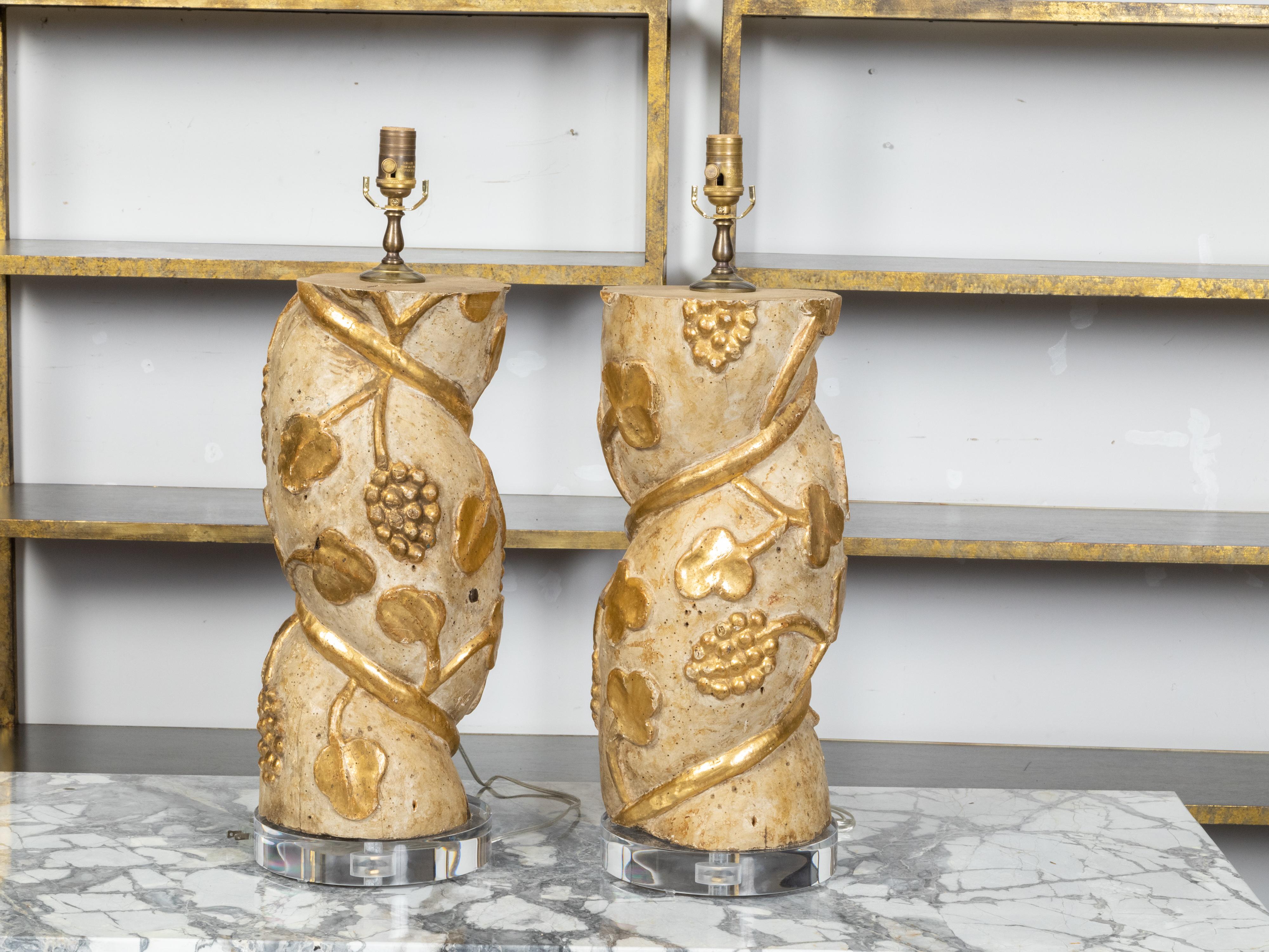 Une paire de fragments de colonnes torsadées italiennes en bois du 18ème siècle, avec des motifs de vigne en bois doré sculpté et des bases rondes en lucite. Créée en Italie au XVIIIe siècle, cette paire de fragments de bois peints en crème présente