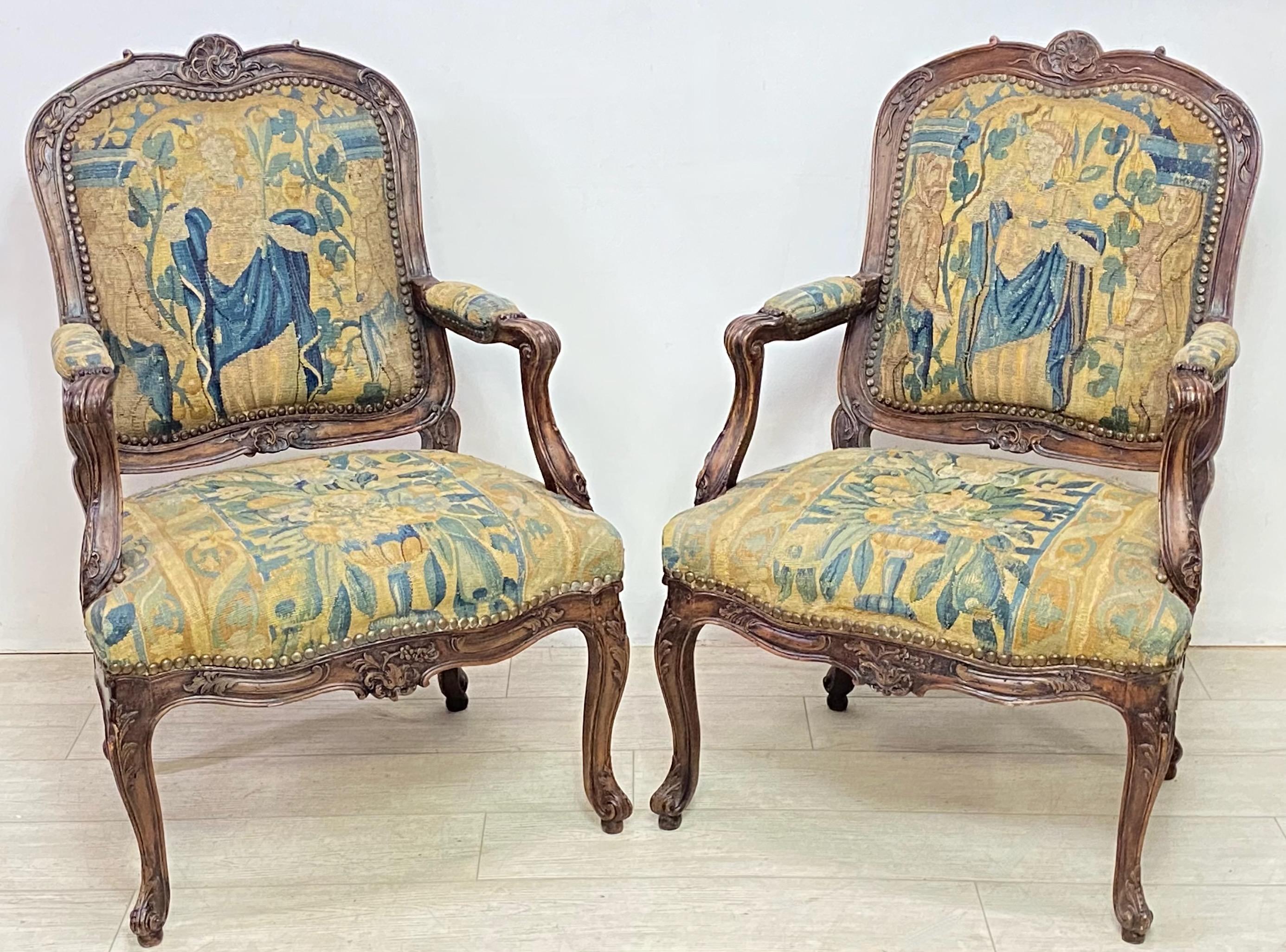 A pair of Louie XV style hand carved walnut chairs with 17th century wool tapestry upholstery. These are of generous proportions, very sturdy and comfortable. The tapestry fabric has been on these chairs since at least the early 20th century.